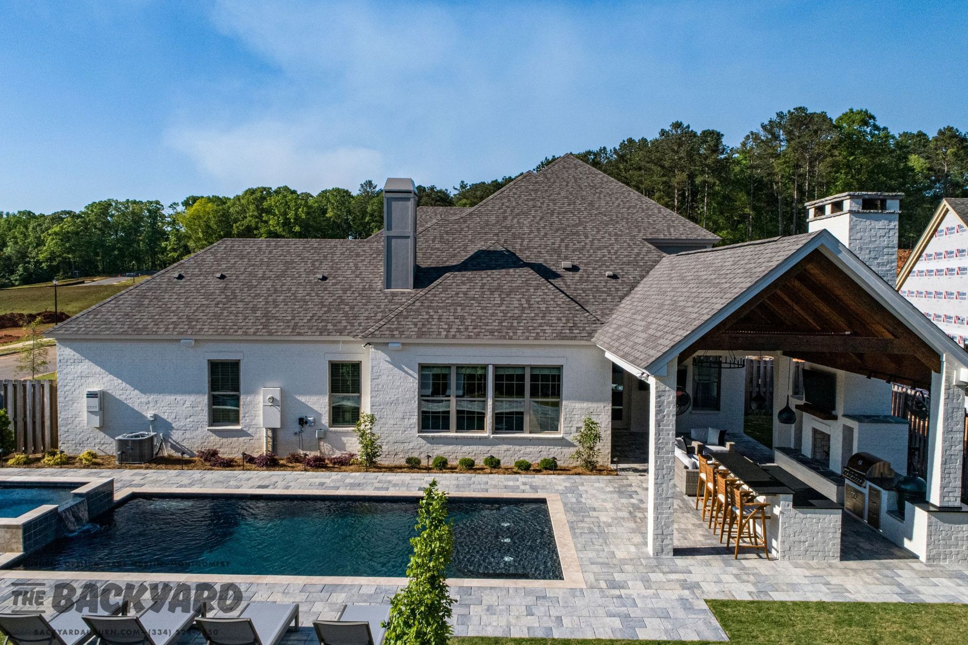 Exterior of a white brick house with a pool and outdoor kitchen.