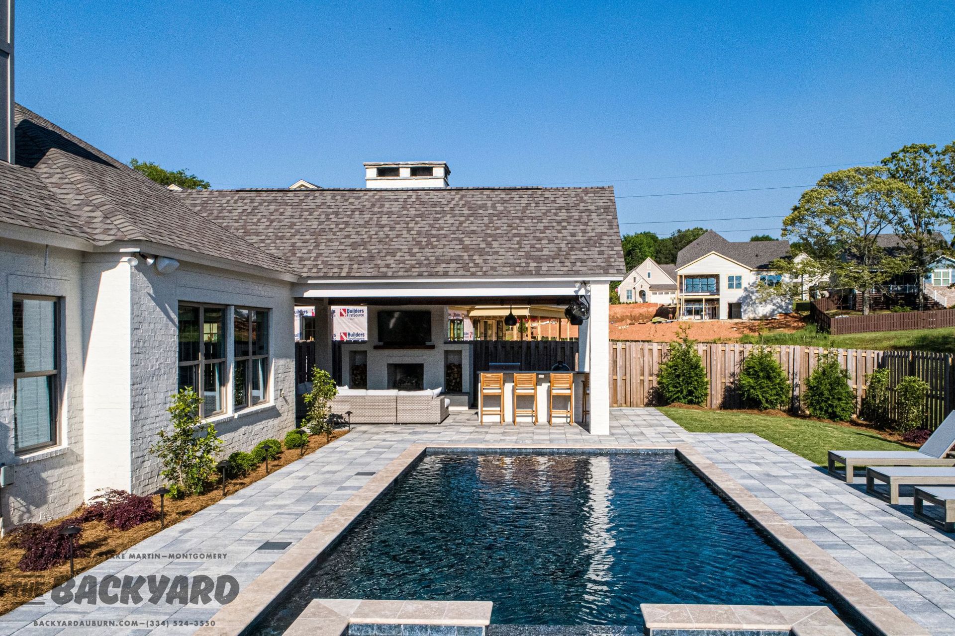 Backyard with rectangular pool, covered patio with bar, and a white house.