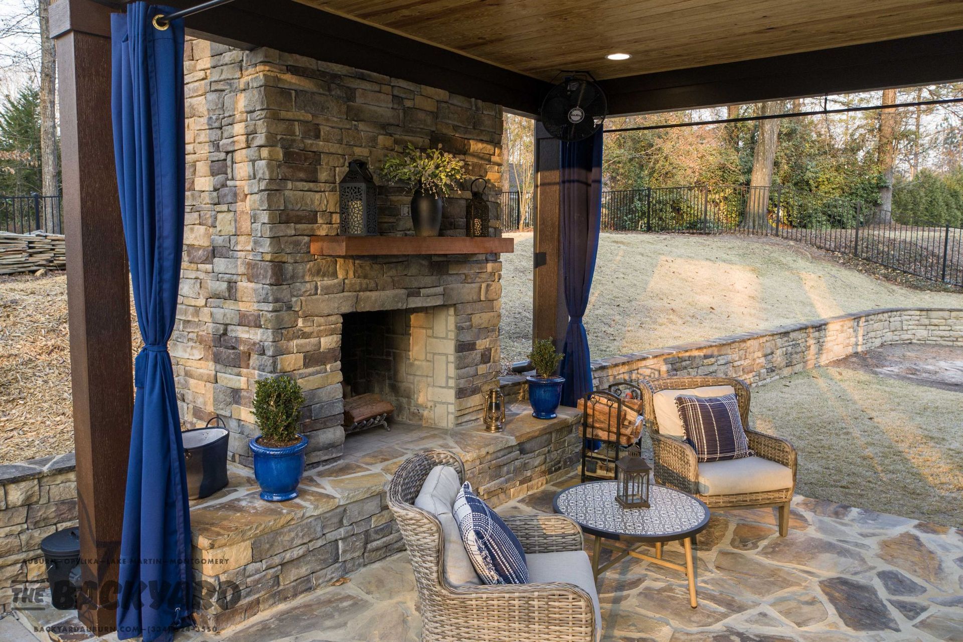 Outdoor patio with a stone fireplace, seating, and blue curtains.