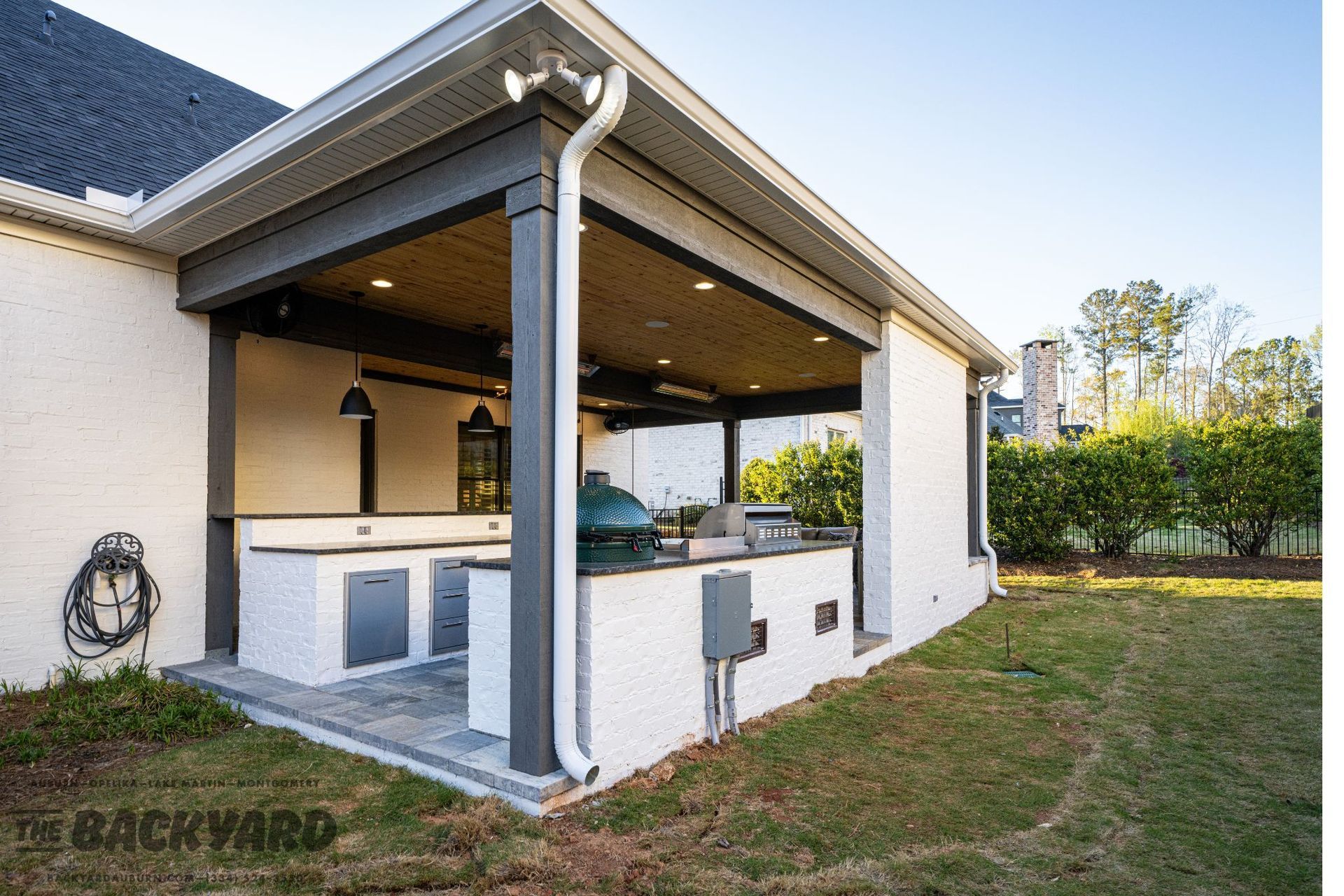 Outdoor kitchen with a white brick exterior, gray trim, and a grill.