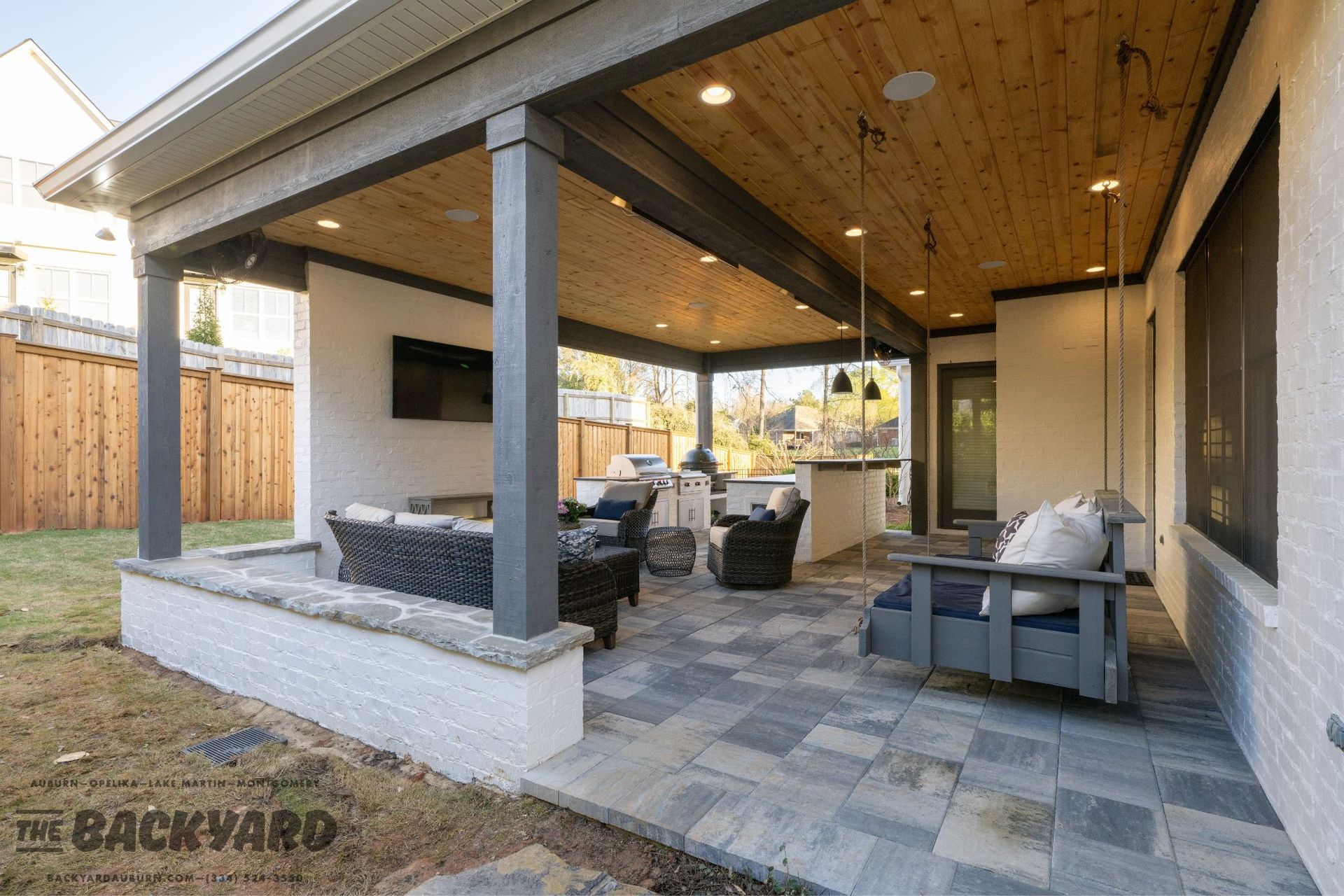 Covered outdoor patio with seating, TV, kitchen area, and wooden ceiling.
