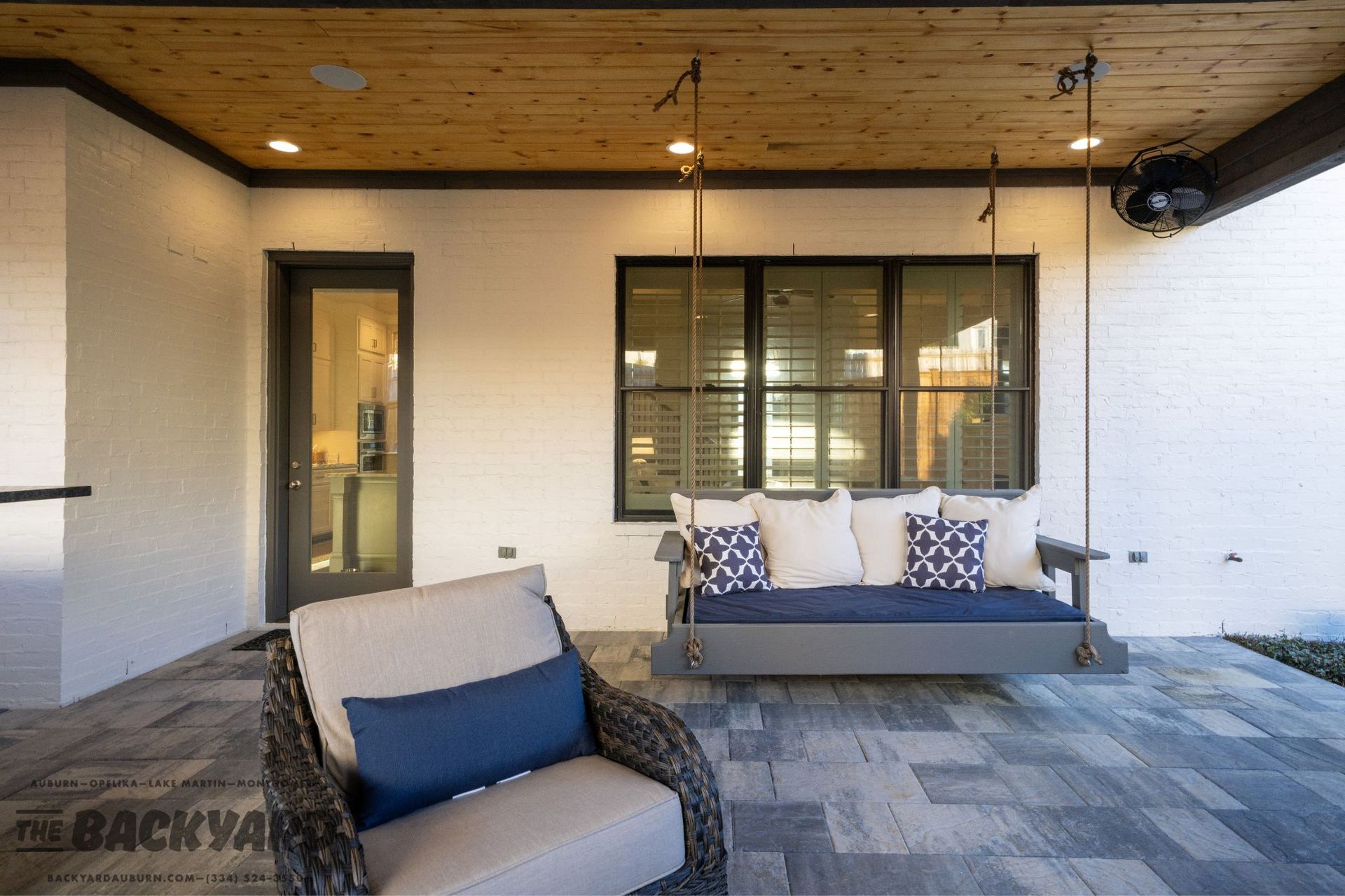 Outdoor patio with a swing and seating, under a wood ceiling, and a stone floor.