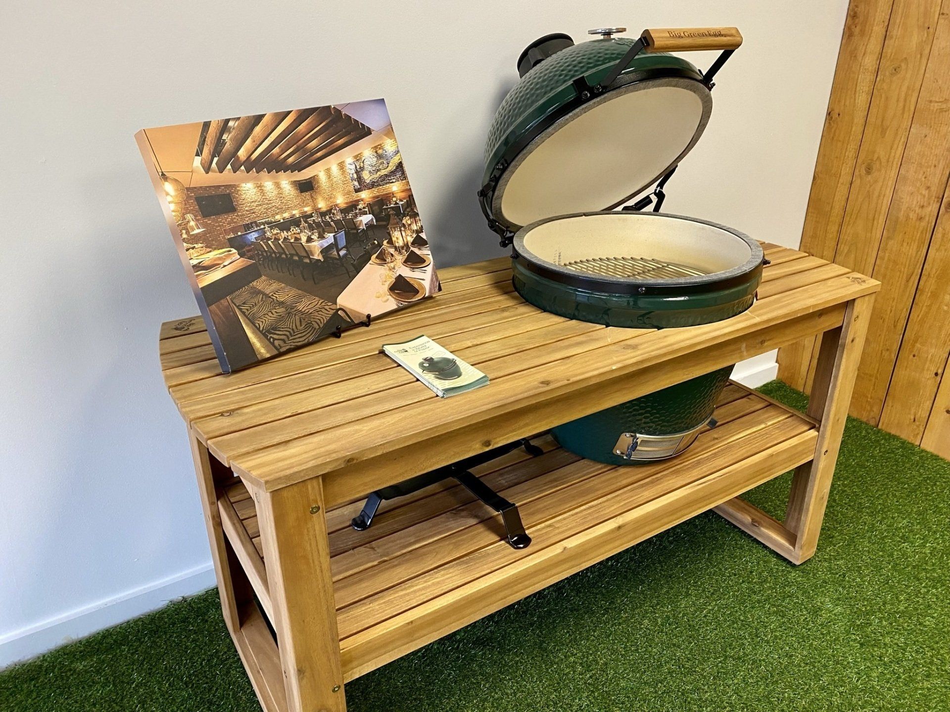 Green Big Green Egg grill on wooden table with cookbook.