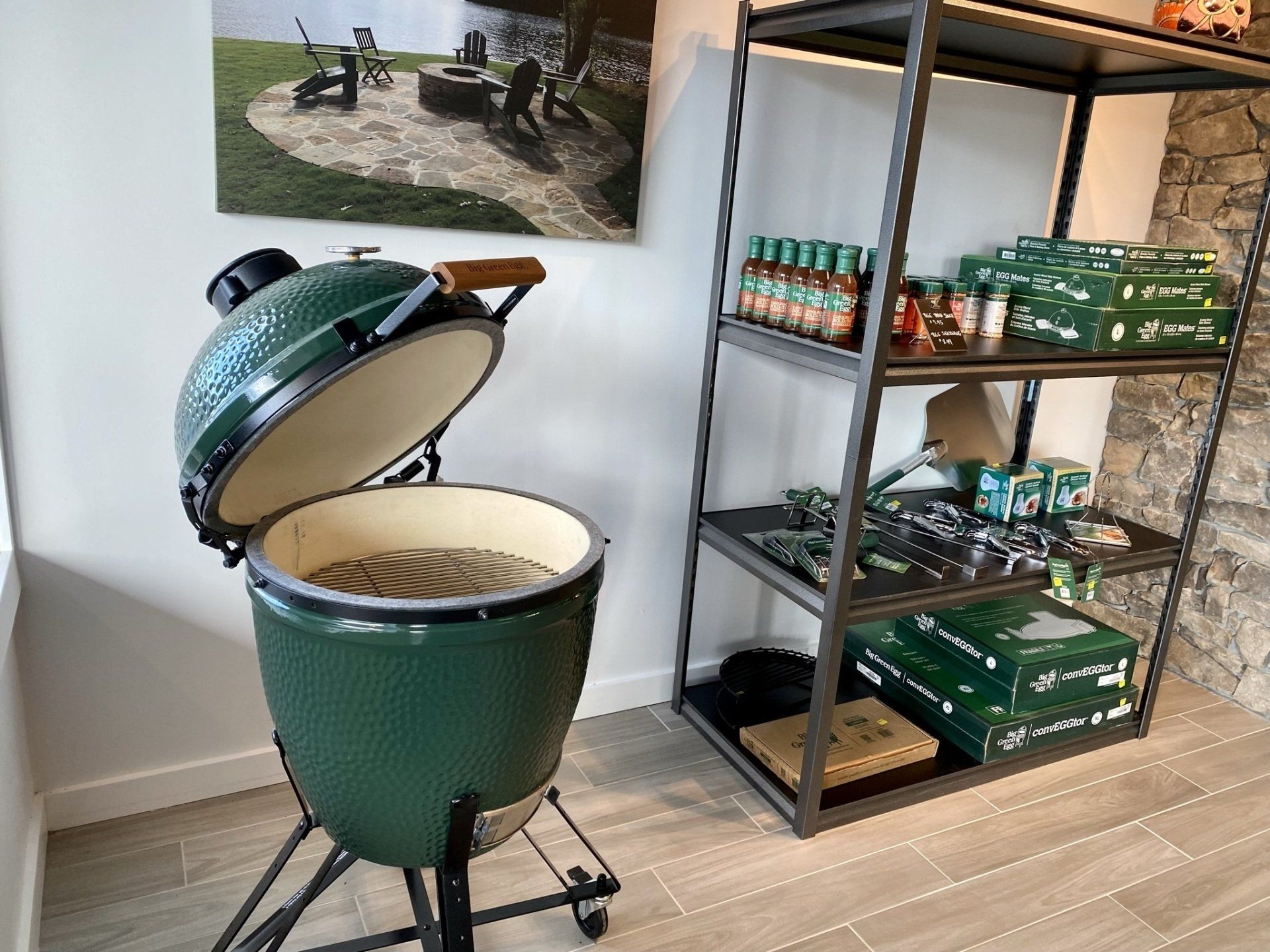 Green Big Green Egg grill with open lid next to shelves of grilling accessories and sauces.