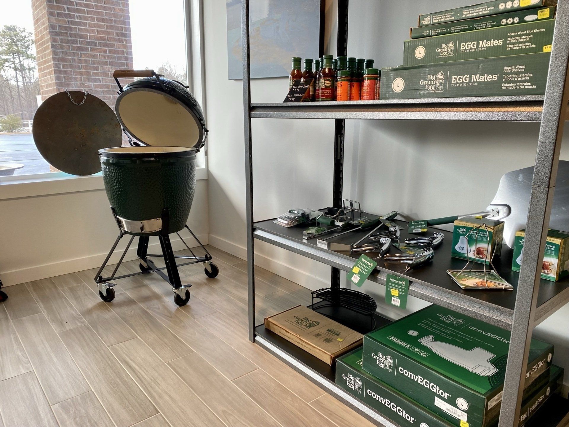 Green ceramic grill next to a shelf of grilling accessories and sauces in a store.