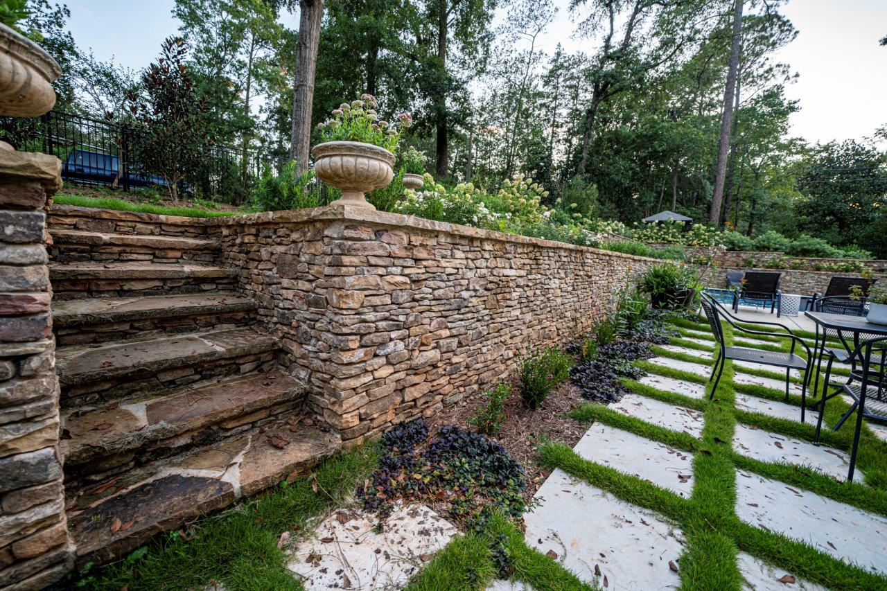 Stone steps leading to a garden with a stone wall, grass pavers, and trees.
