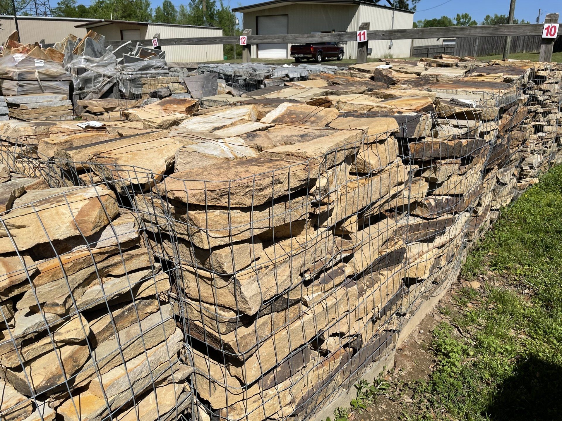 Stacks of light brown flagstone in wire cages, outdoors.