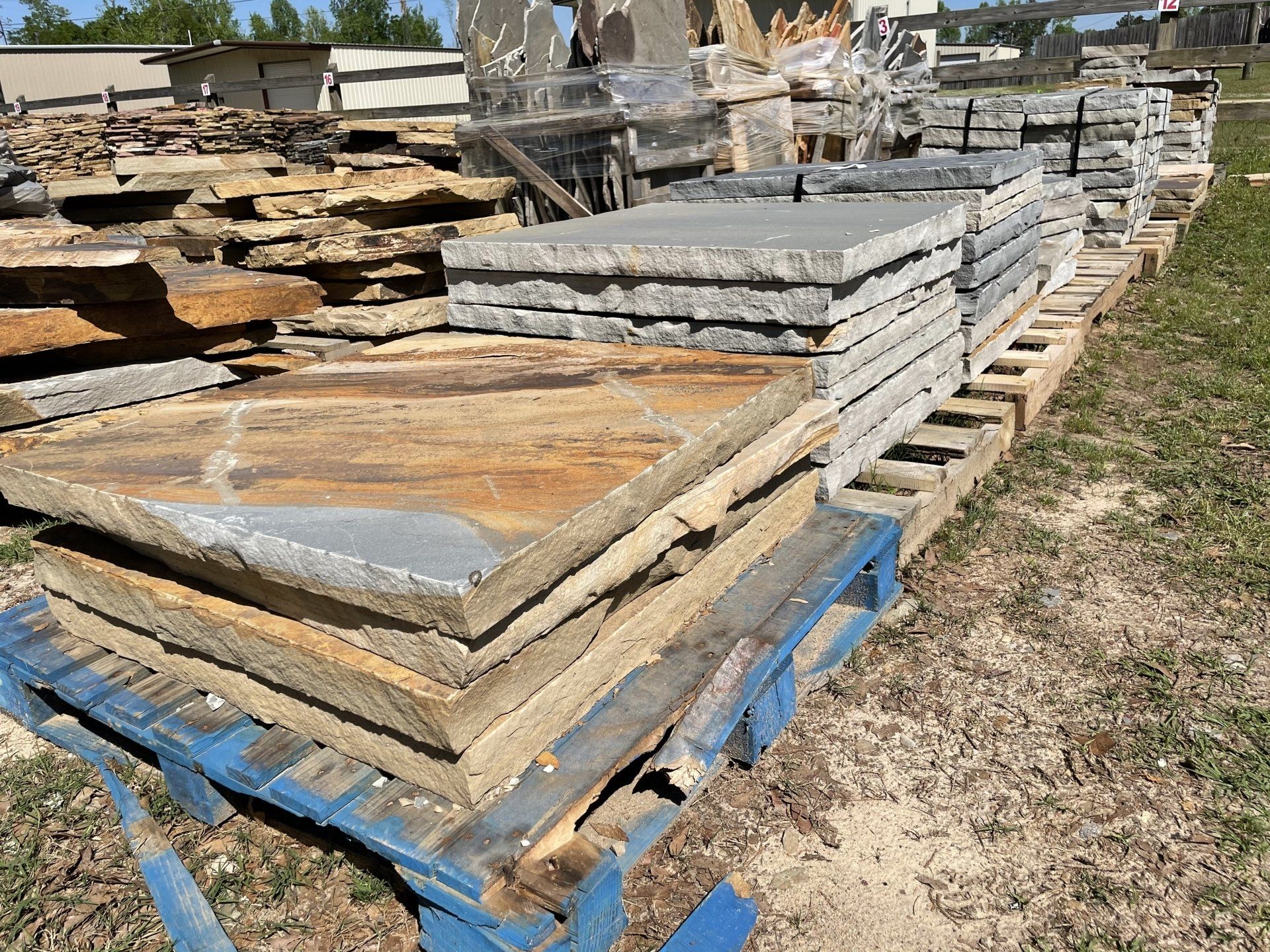 Stone slabs stacked on pallets, outdoors. Varying colors of brown and gray.