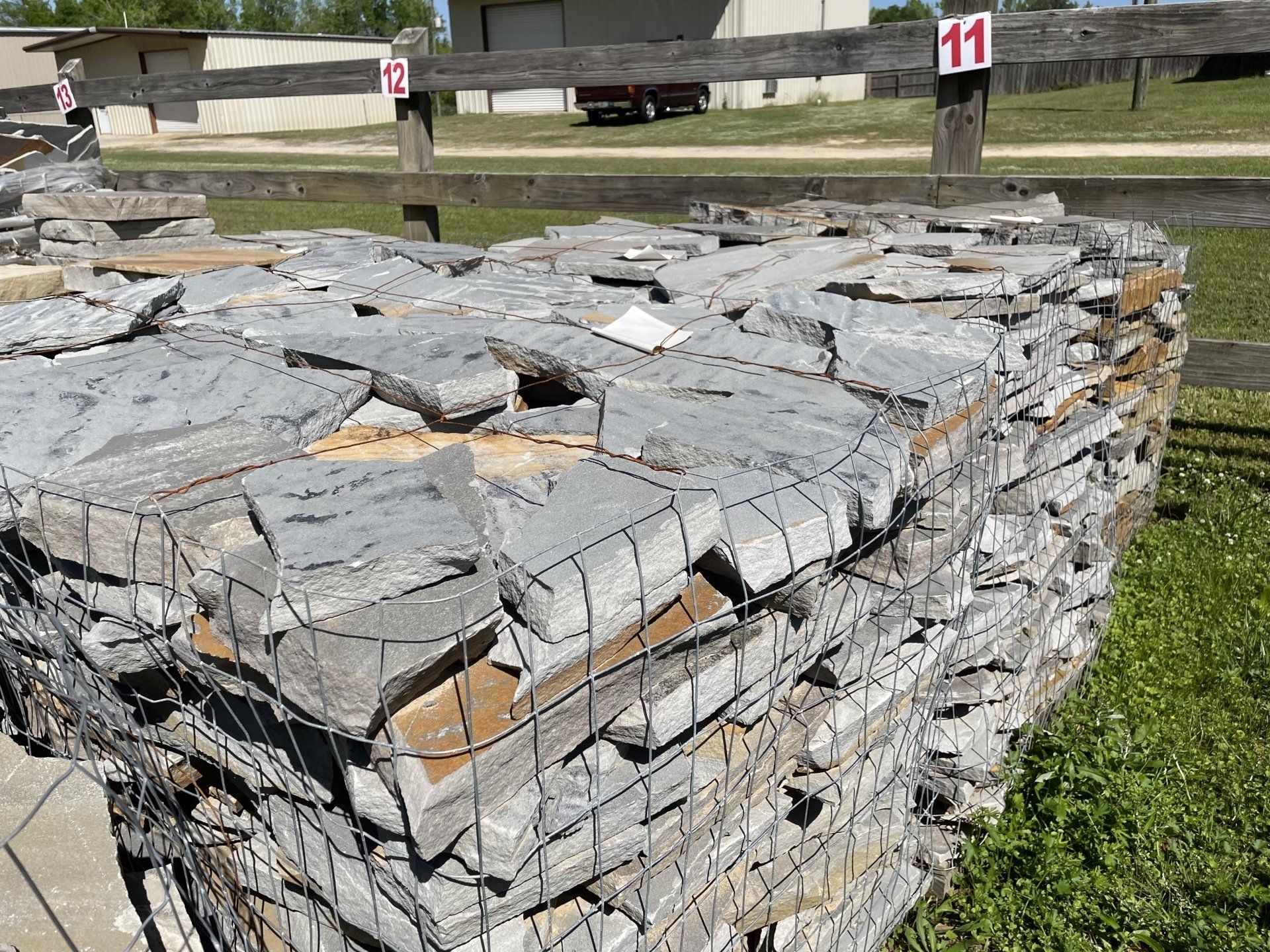 Stack of gray stone pieces bound by wire mesh. Outdoors, numbered sign, green grass.