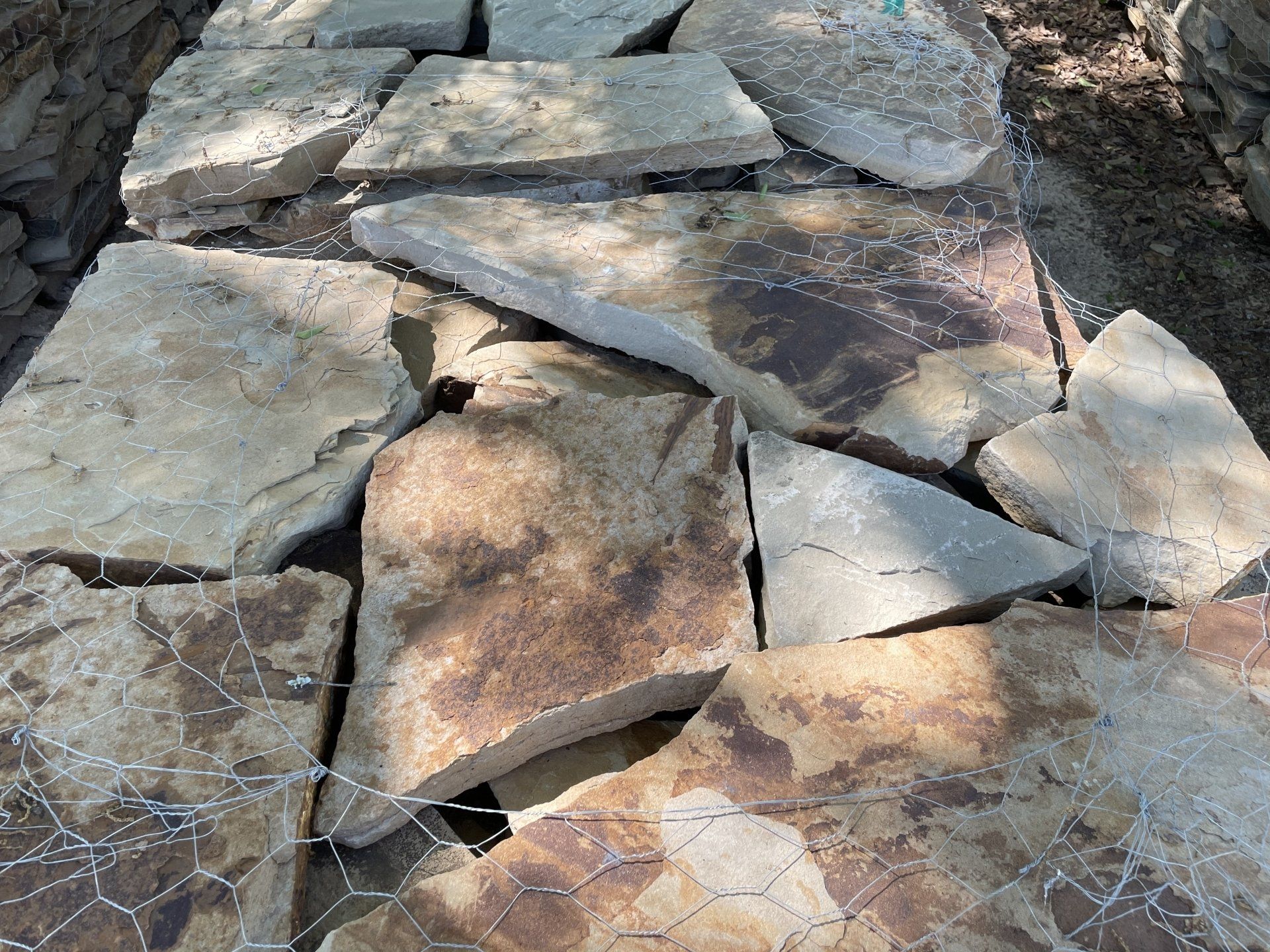Flagstone pathway under construction, stones in shades of tan and brown resting on wire mesh.