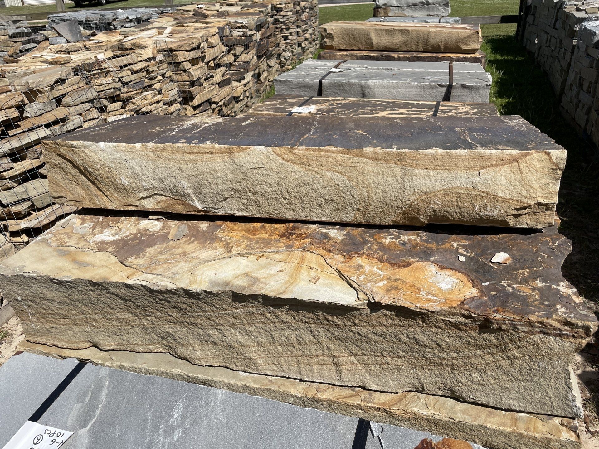 Two stacked, rough-hewn sandstone blocks with tan and brown hues, in an outdoor stone yard.