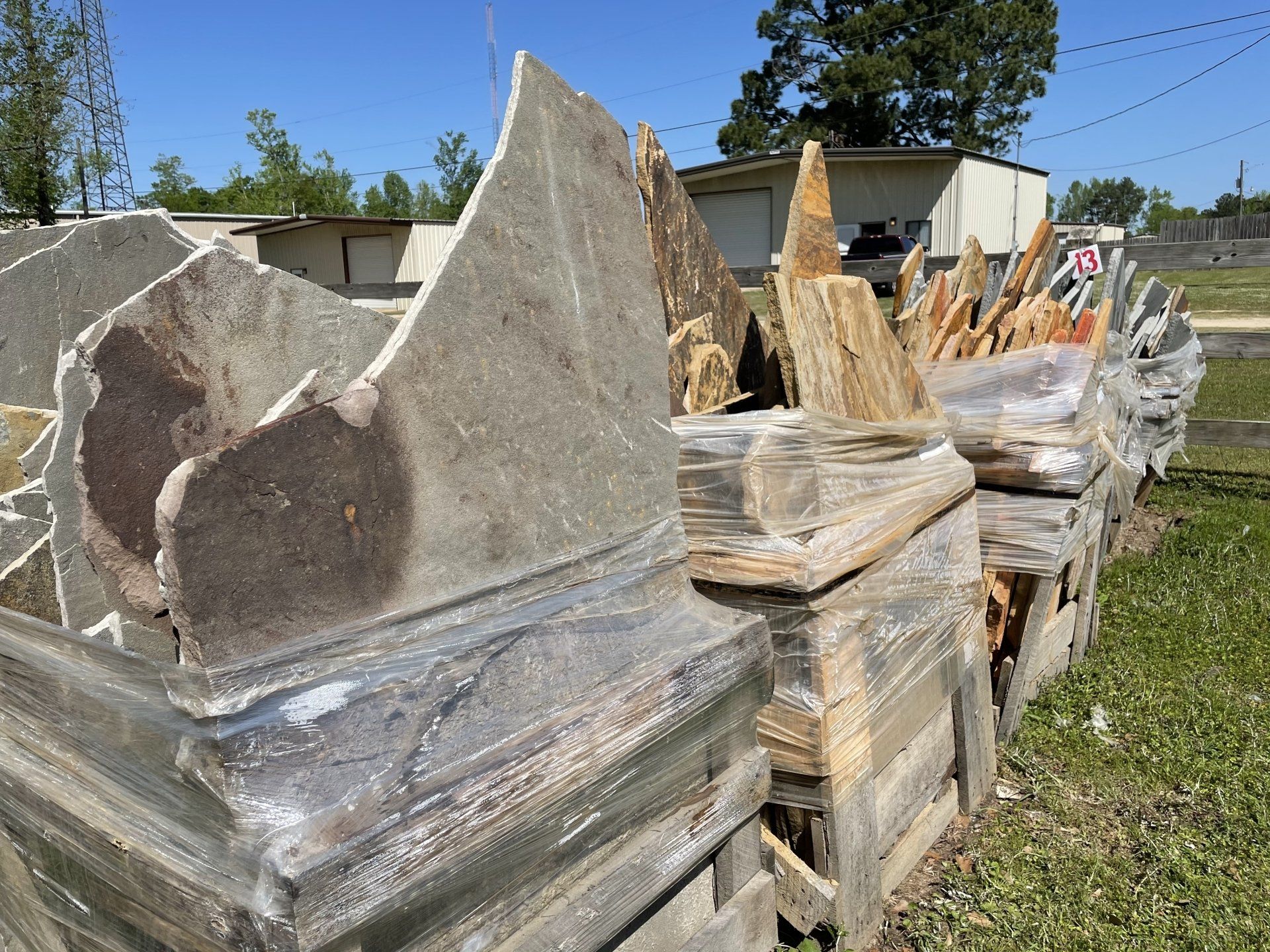 Stone slabs stacked on pallets outside, various shapes and colors, ready for sale.