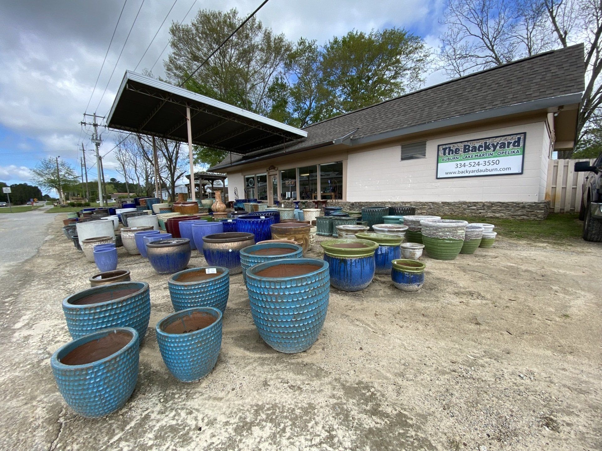 Outdoor store displays various blue, green, and brown ceramic pots; building with a sign: 