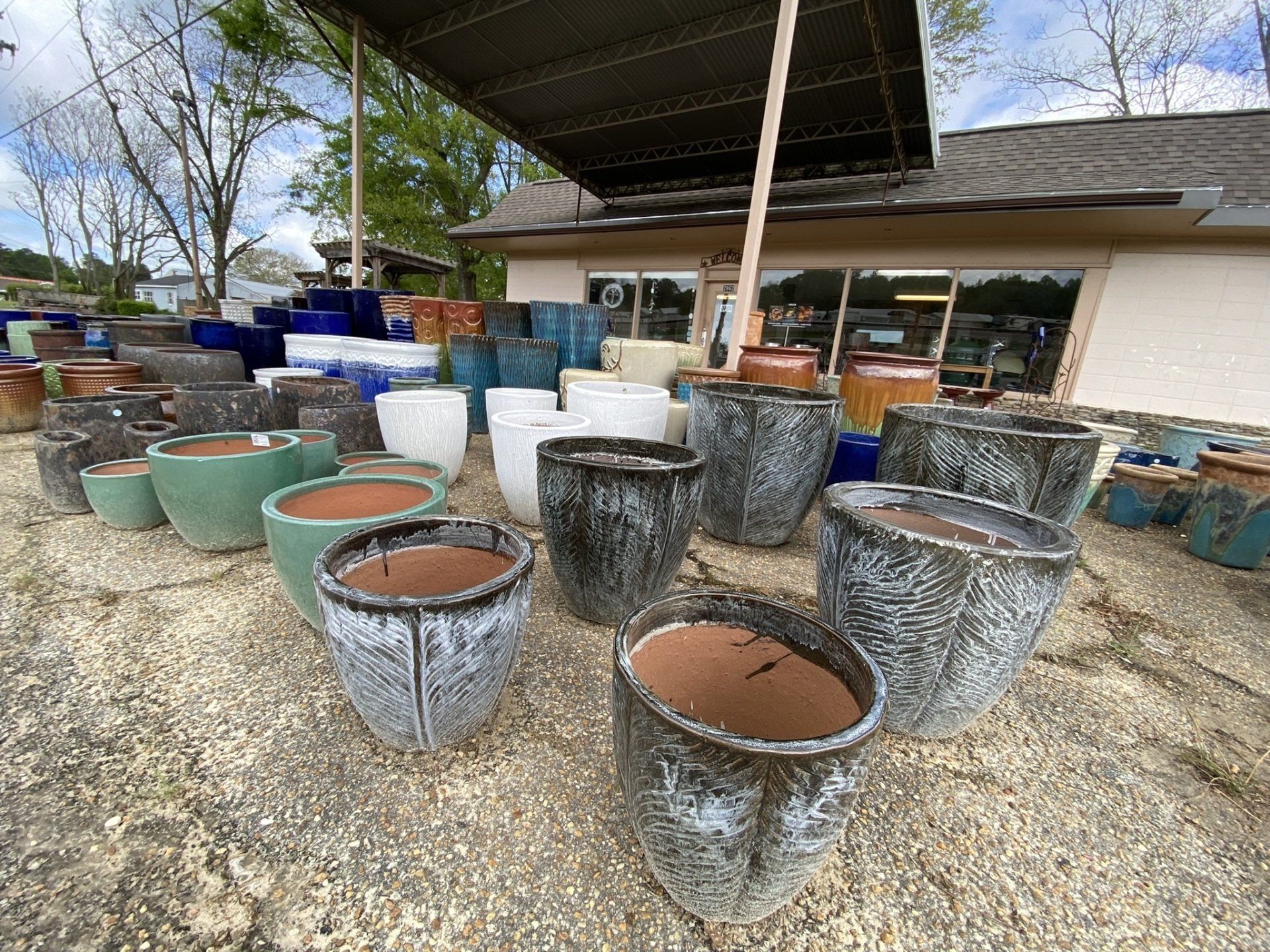 Assorted ceramic pots of various colors and sizes are displayed outside a shop on gravel.