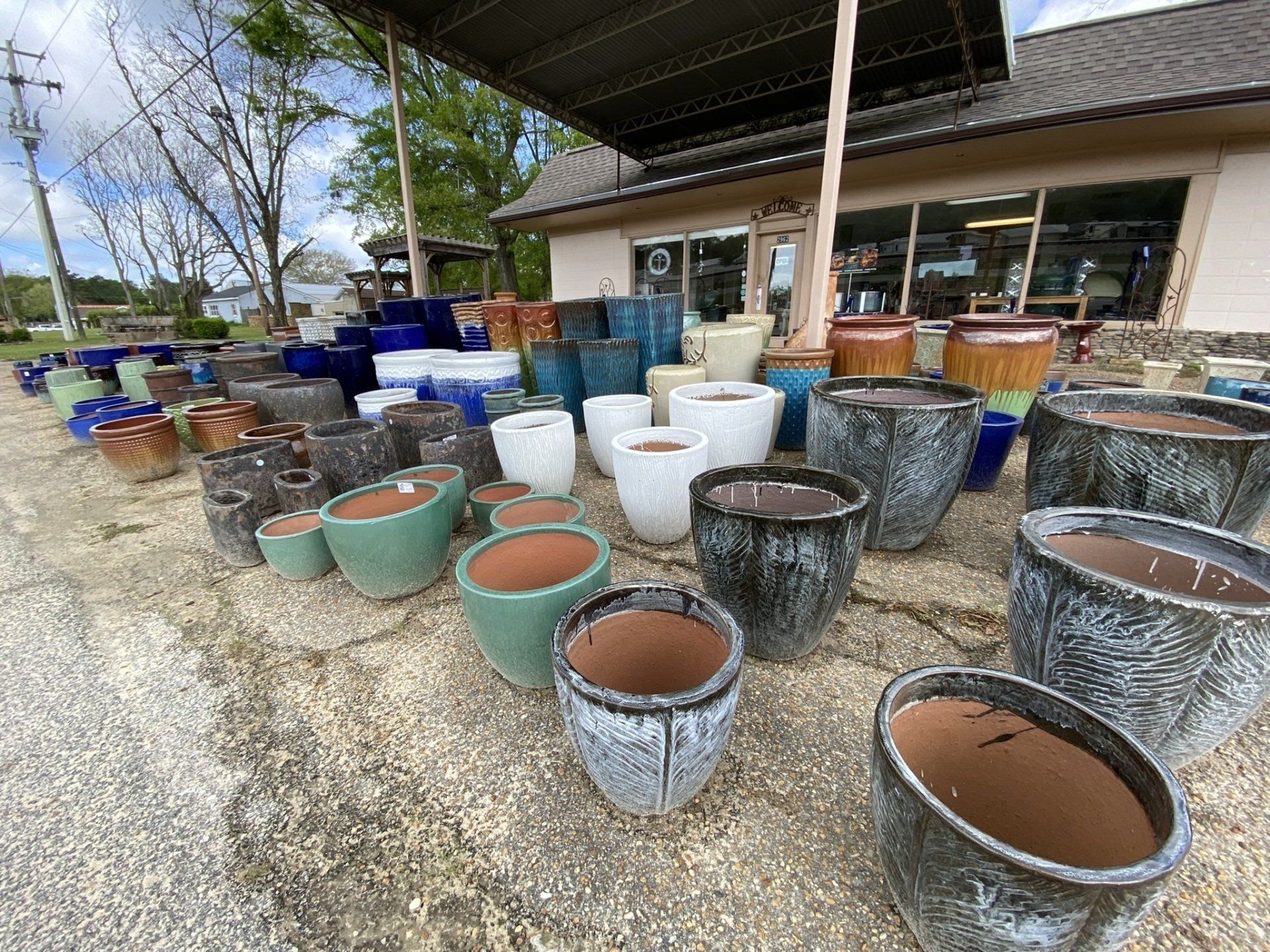 A variety of ceramic pots for sale at a garden center, displayed outside on a cracked pavement.