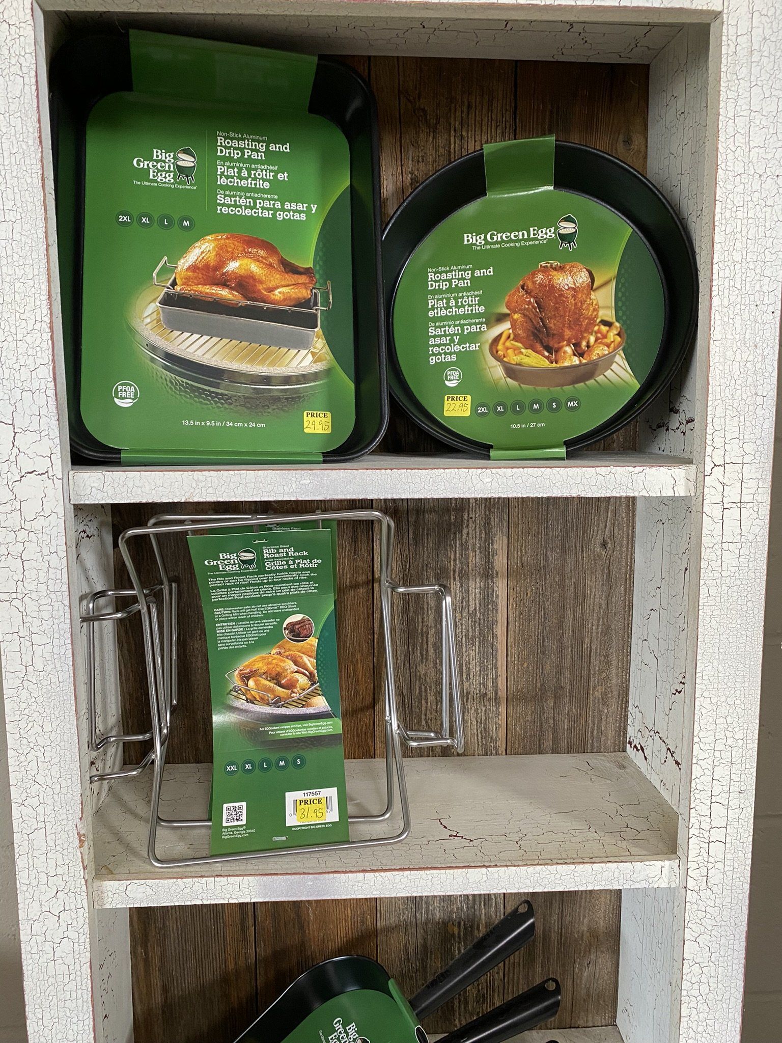 Shelves with cooking equipment: roasting pans, a wire rack, and accessories; all in green packaging.