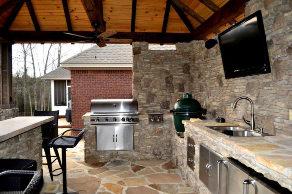 An outdoor kitchen with a grill , sink , and television.