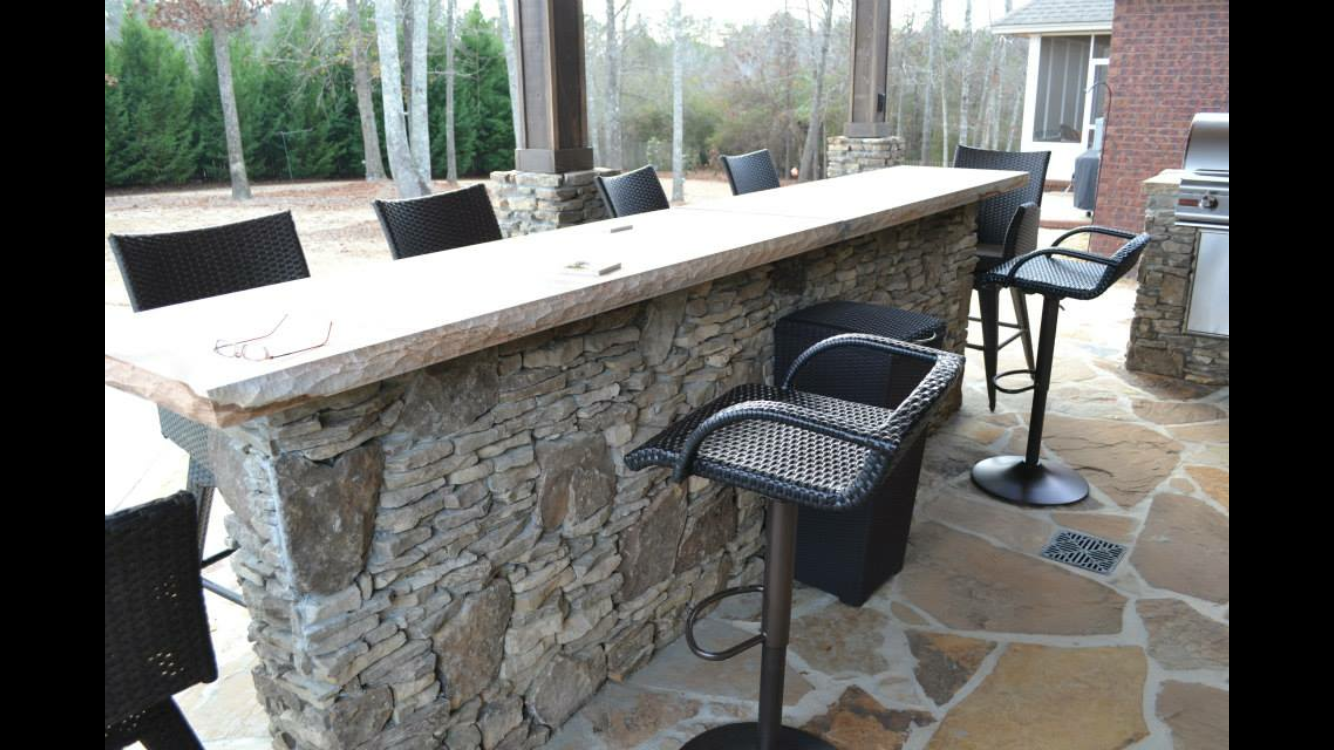A stone bar with wicker chairs and a grill