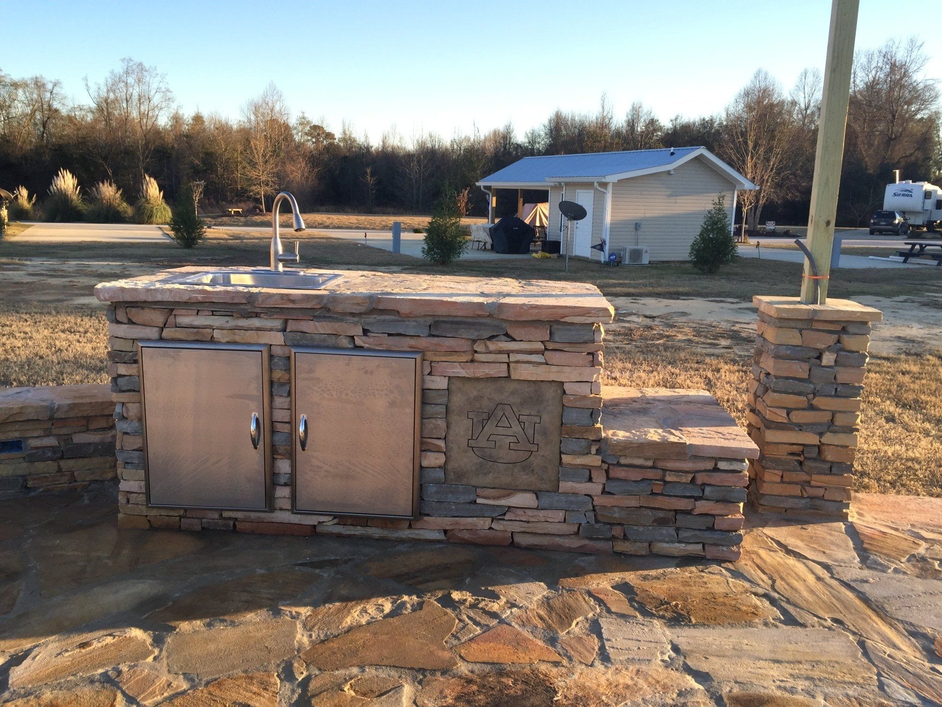 A stone kitchen with a sink and cabinets in front of a house