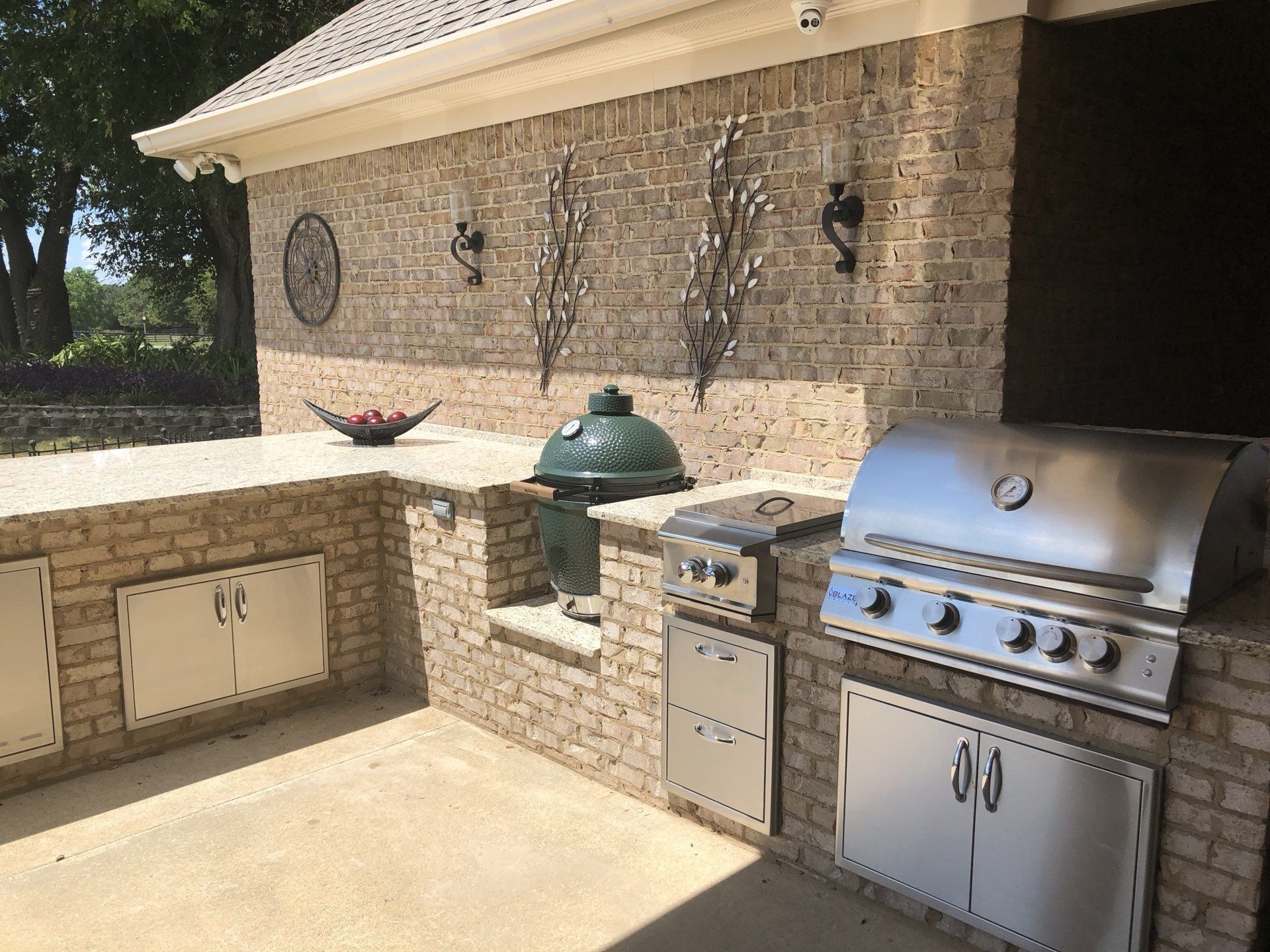 An outdoor kitchen with a green egg grill and a stainless steel grill.