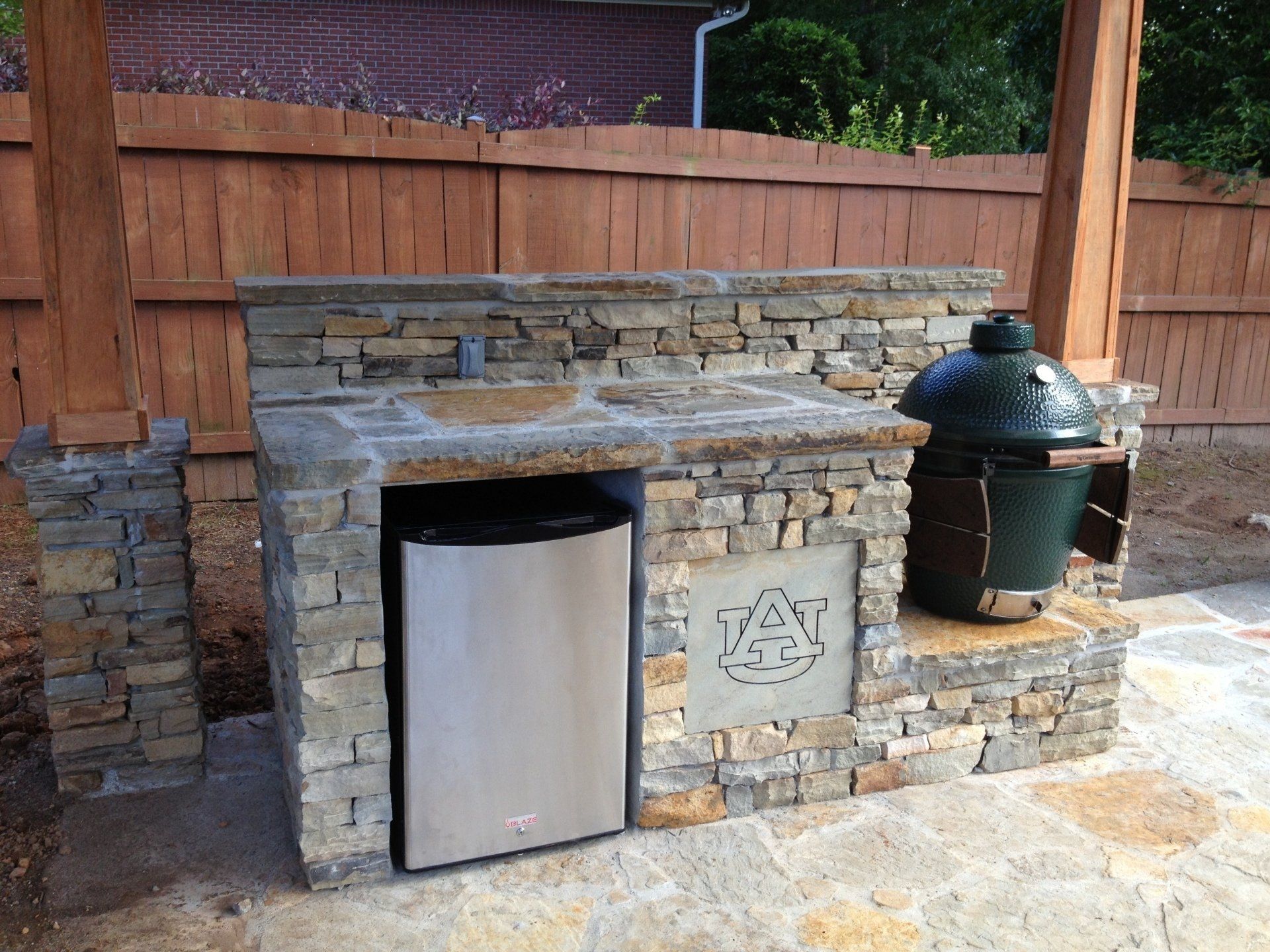 An outdoor kitchen with a stainless steel refrigerator and a big green egg