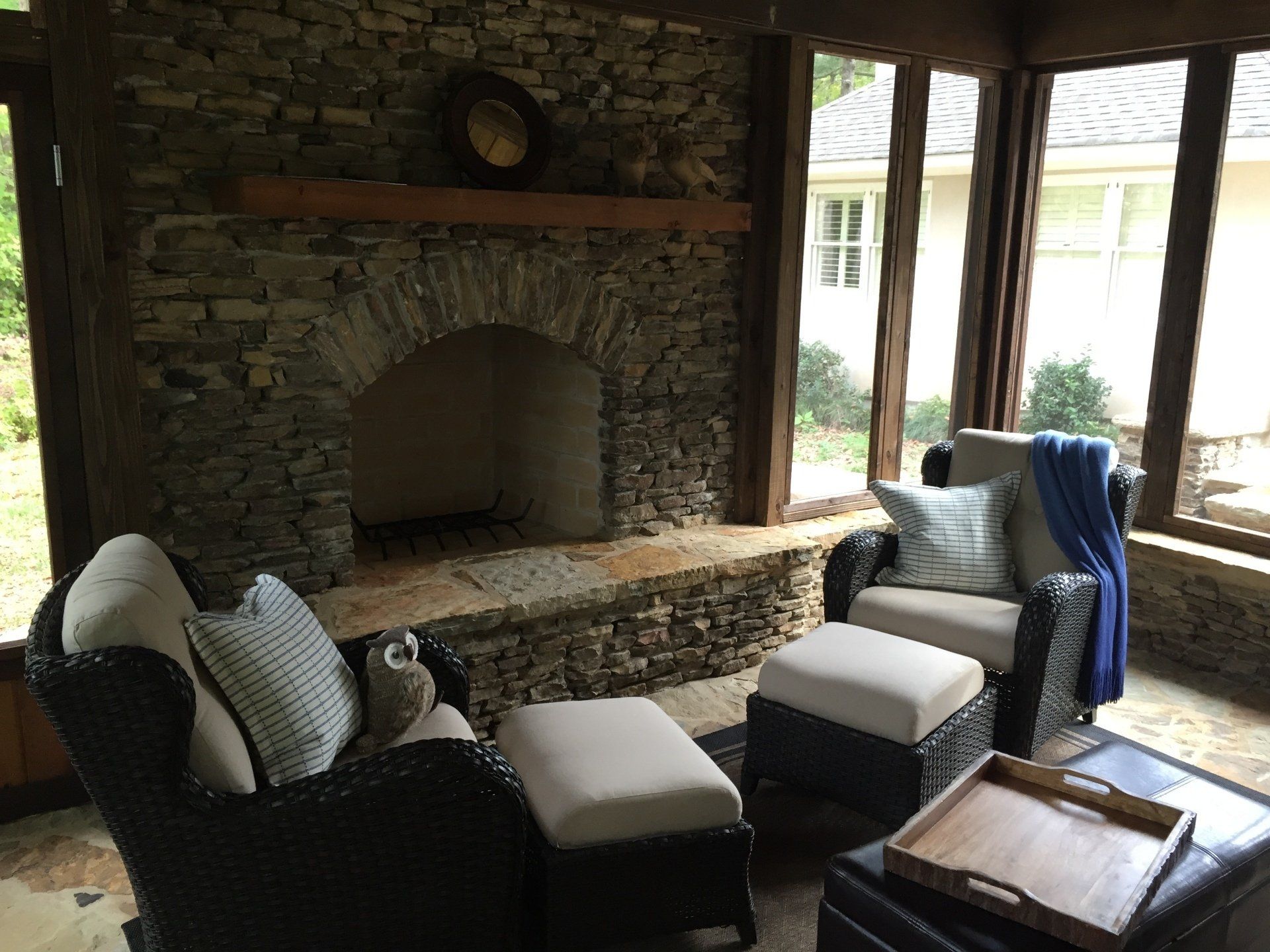 Stone fireplace in a sunroom with wicker chairs, ottomans, and a view of the outdoors.