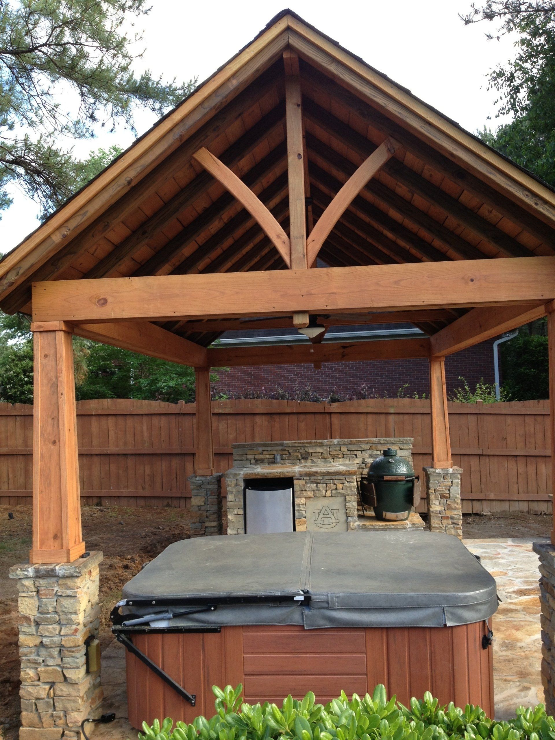 Wooden gazebo with hot tub, outdoor kitchen, and stone accents.