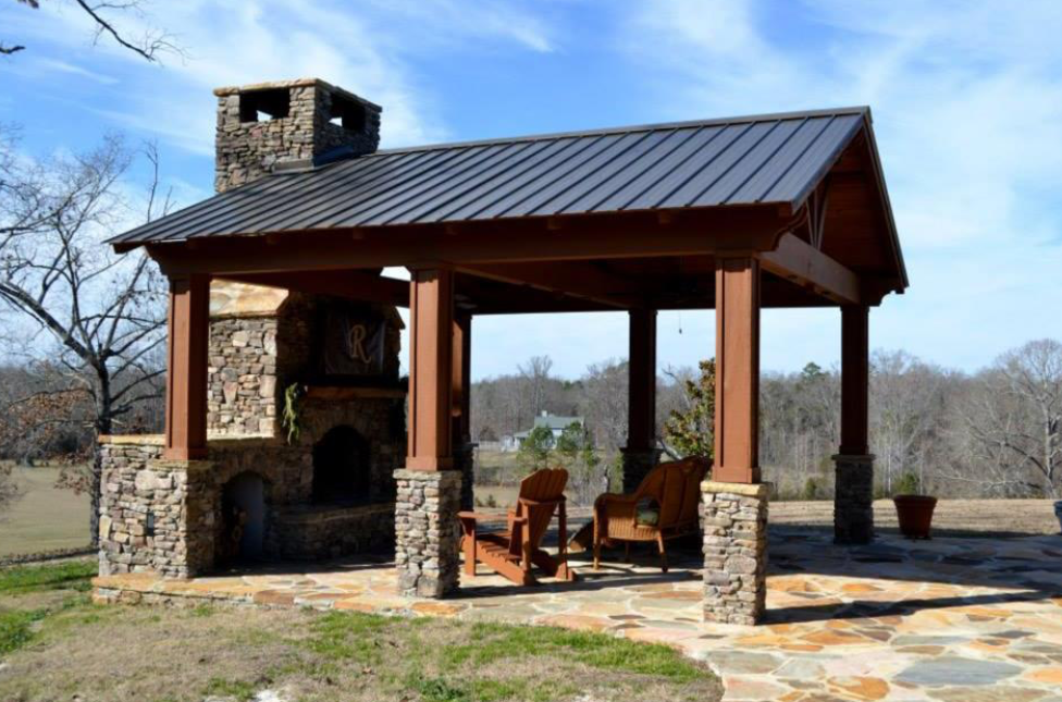 Outdoor pavilion with stone fireplace, wooden frame, metal roof, and seating.
