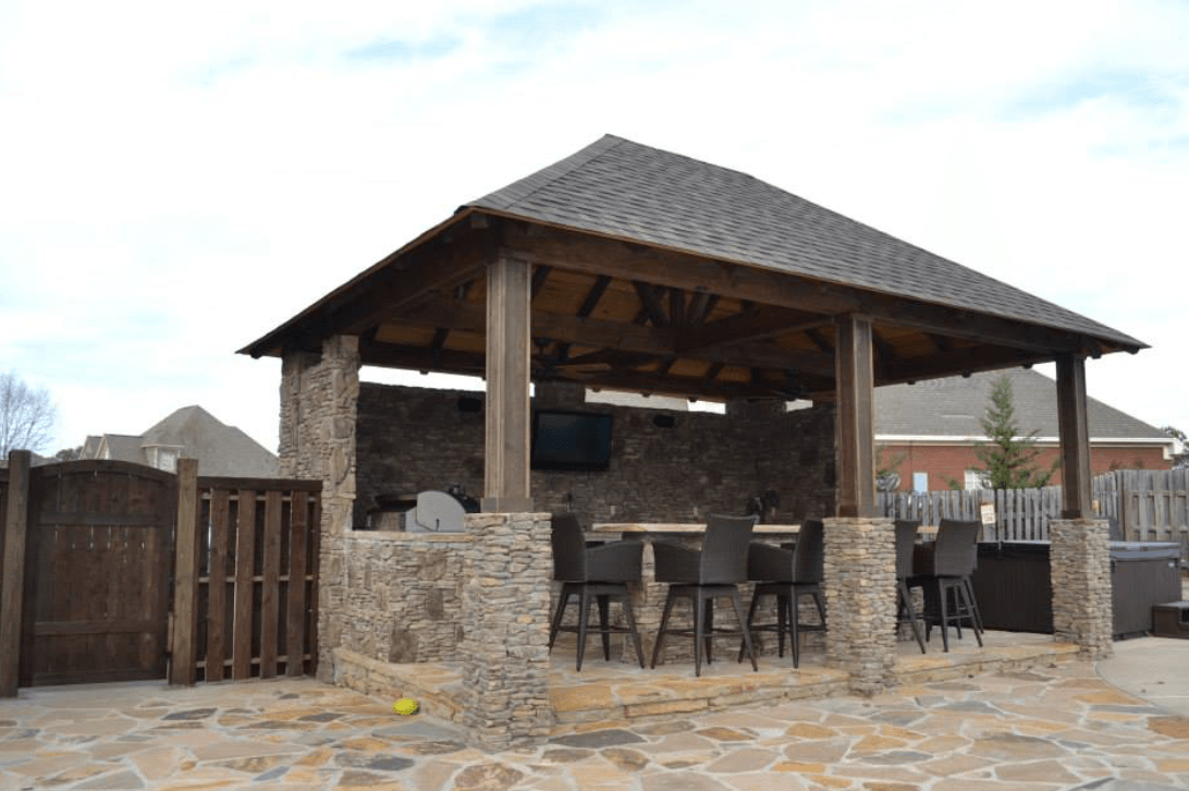 Outdoor bar with stone columns, wooden roof, and chairs on a stone patio.