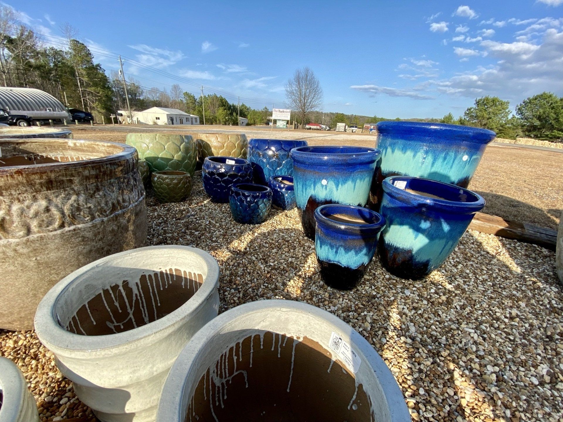 Various ceramic pots in shades of blue and gray on a gravel ground outdoors.