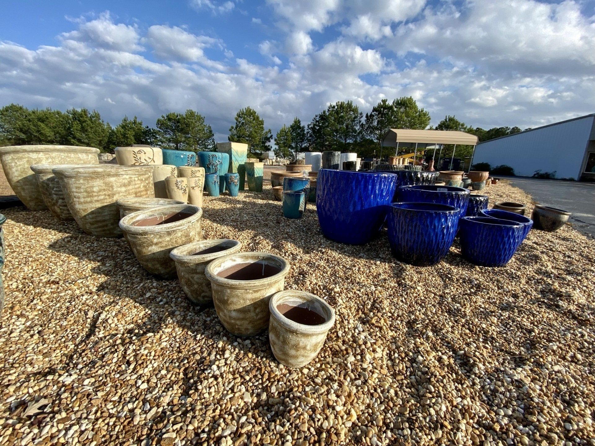 Assortment of colorful ceramic planters on a gravel lot under a cloudy sky.