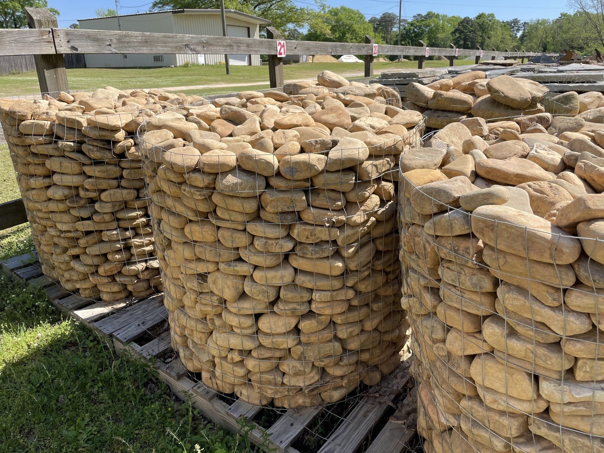 Three cylindrical wire baskets filled with beige stones on wooden pallets outdoors.