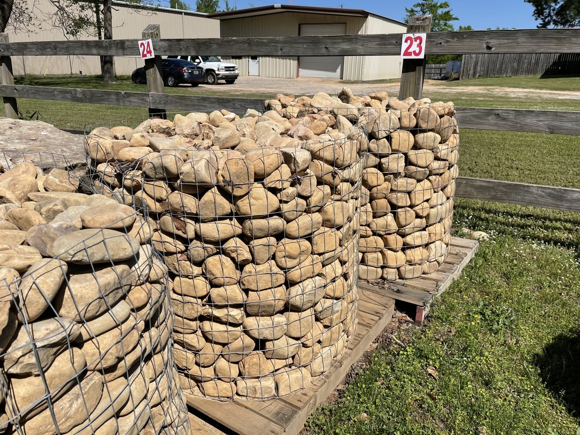 Three cylindrical wire baskets filled with tan river rocks, outdoors.