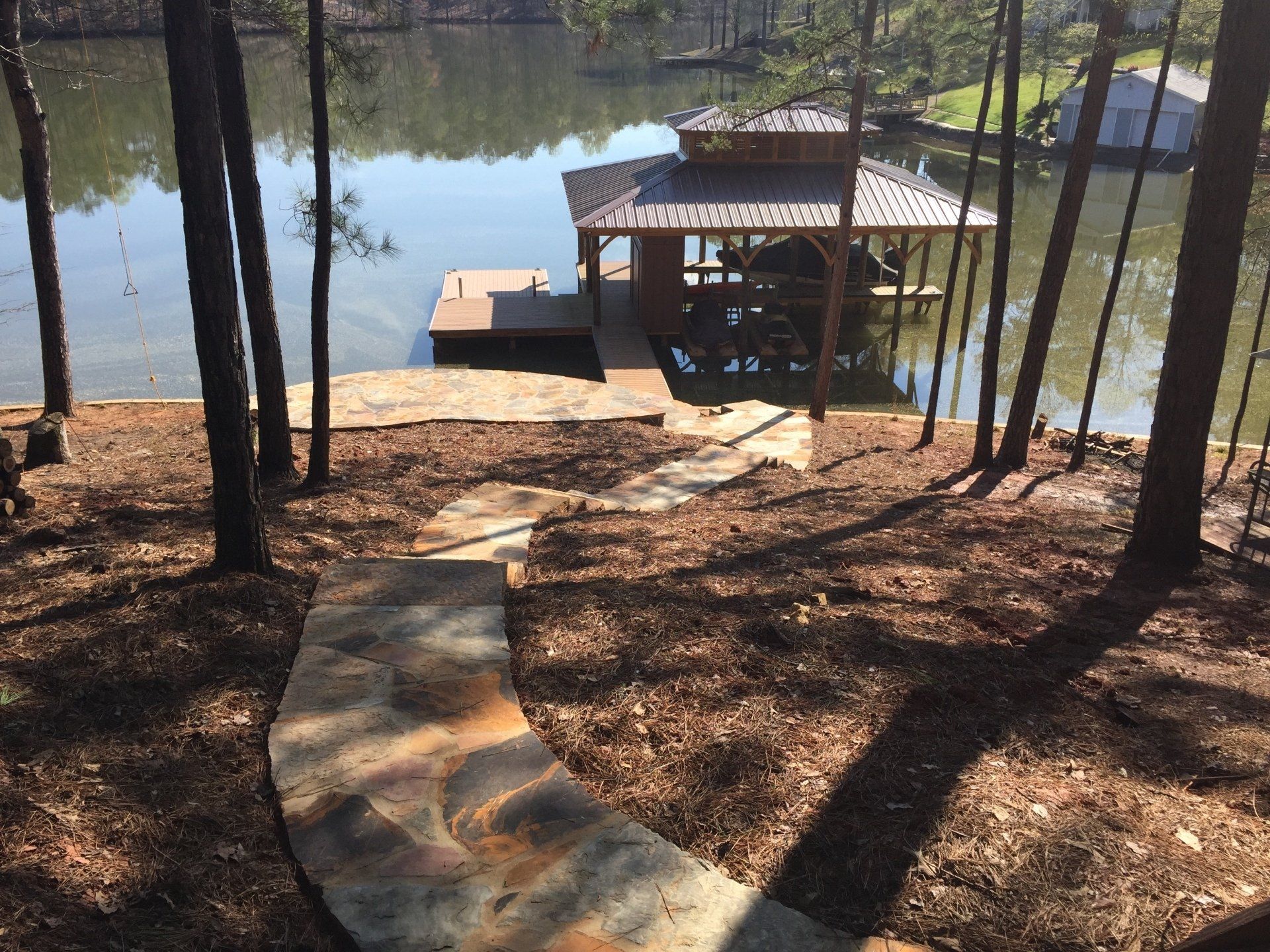 Stone path leads down to a lake and boat dock shaded by a wooden structure.
