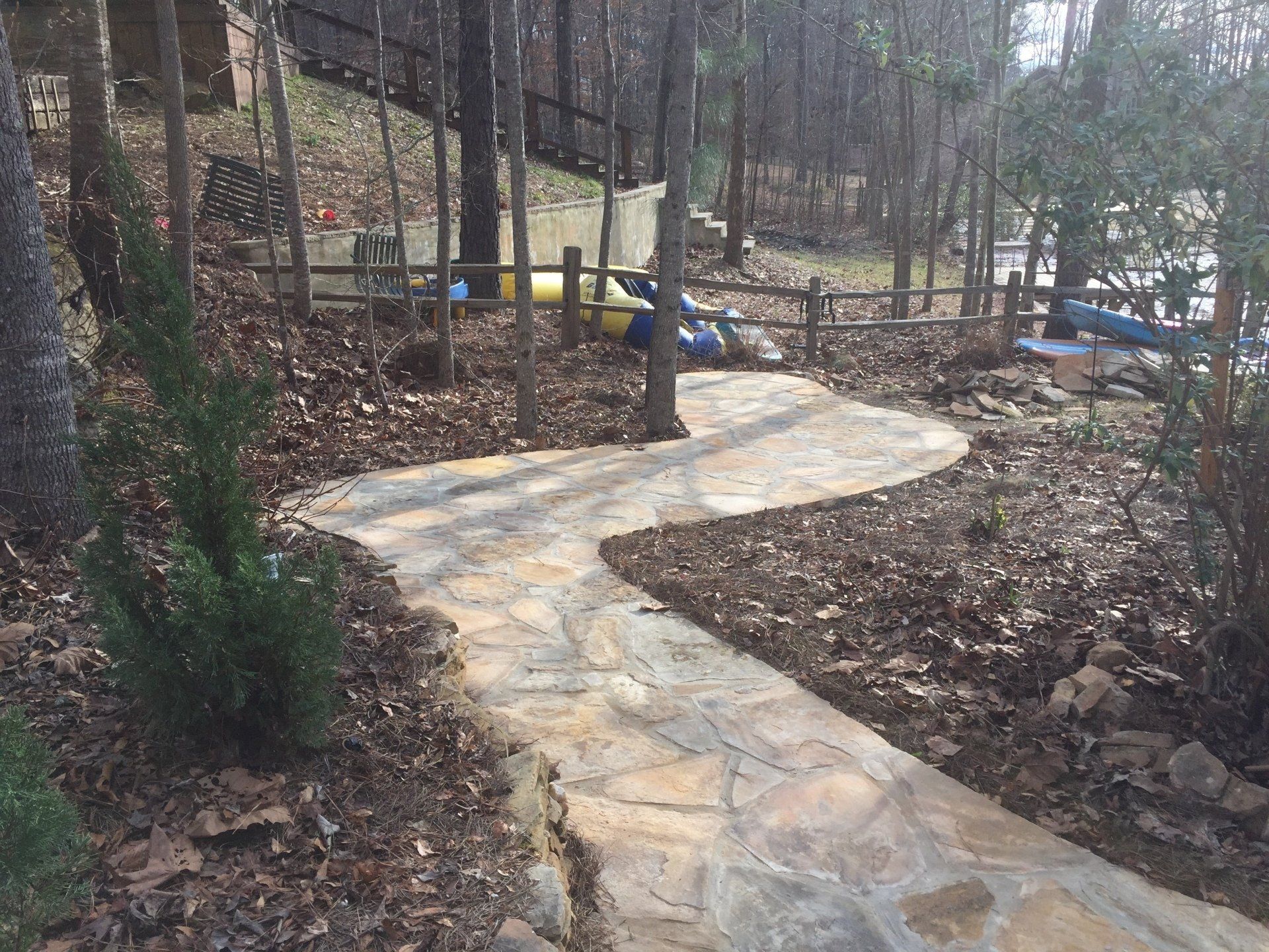 A stone path winds through a wooded area. Bare trees and brown leaves surround the path.