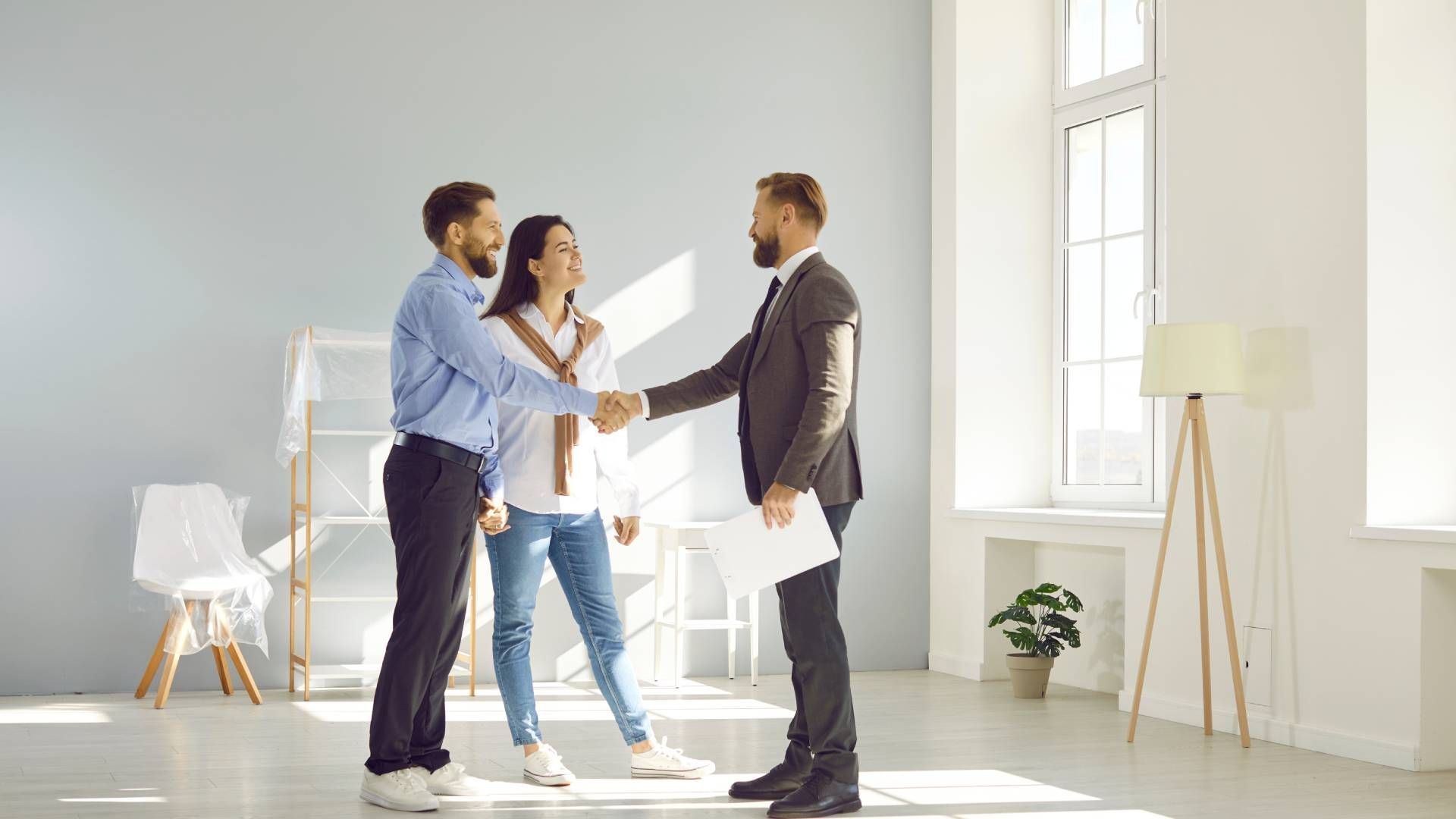 A man and woman are shaking hands with a real estate agent in an empty room.