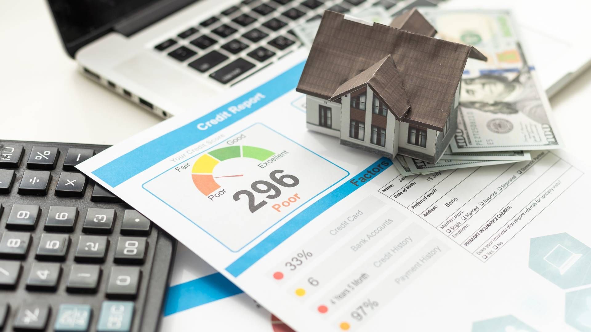 A model house is sitting on top of a piece of paper next to a calculator and a laptop.