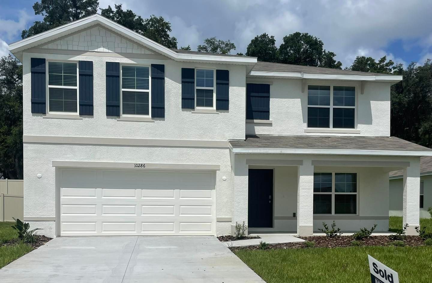 A white house with black shutters and a sold sign in front of it.