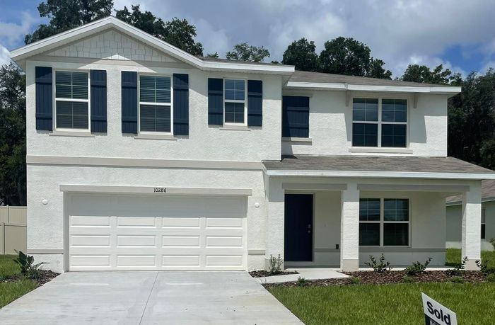 A white house with black shutters and a sold sign in front of it.