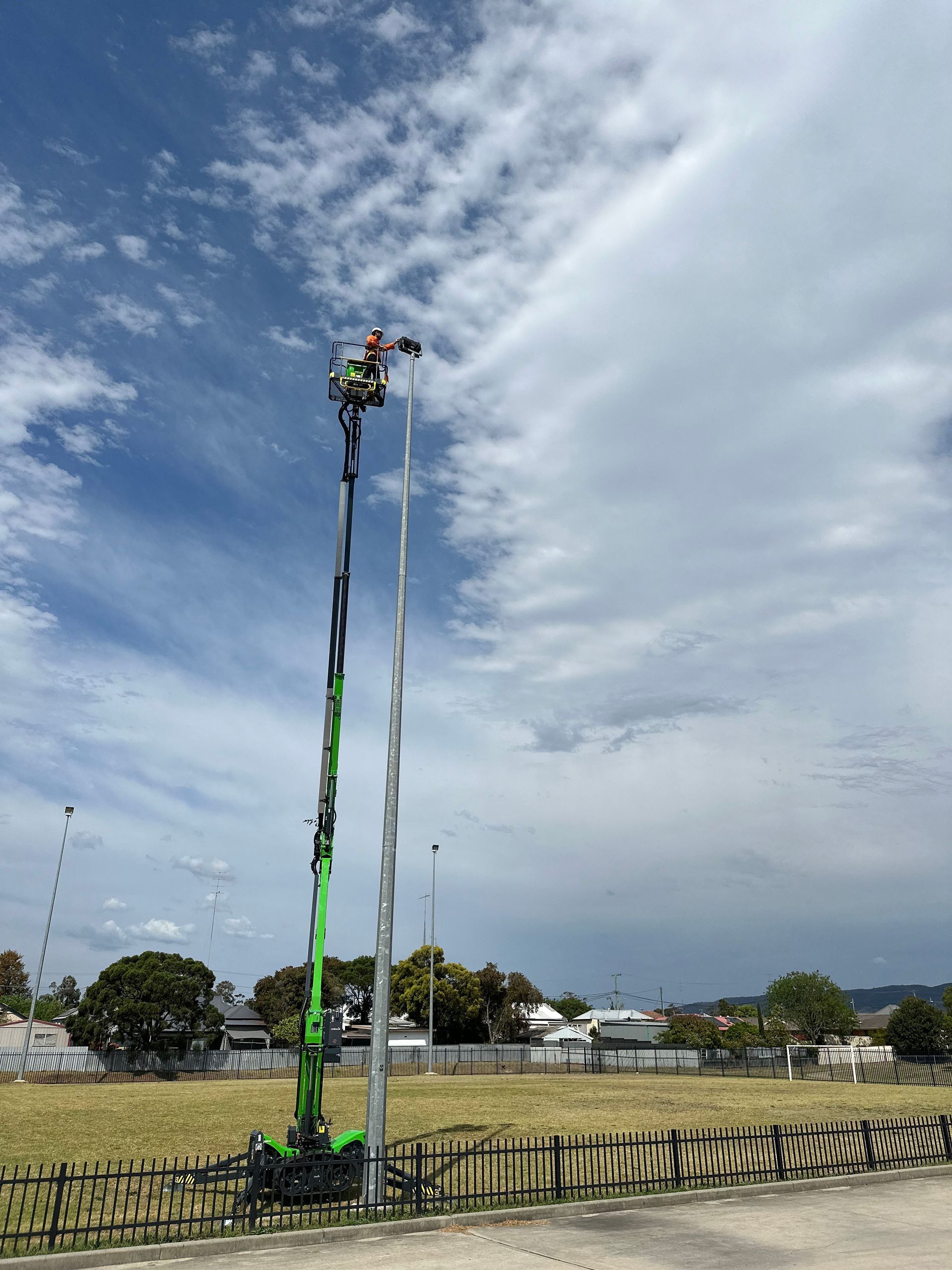 A Green Crane Is Holding A Man While Fixing A Tall Light Post — High Work Services in Hunter Valley, NSW