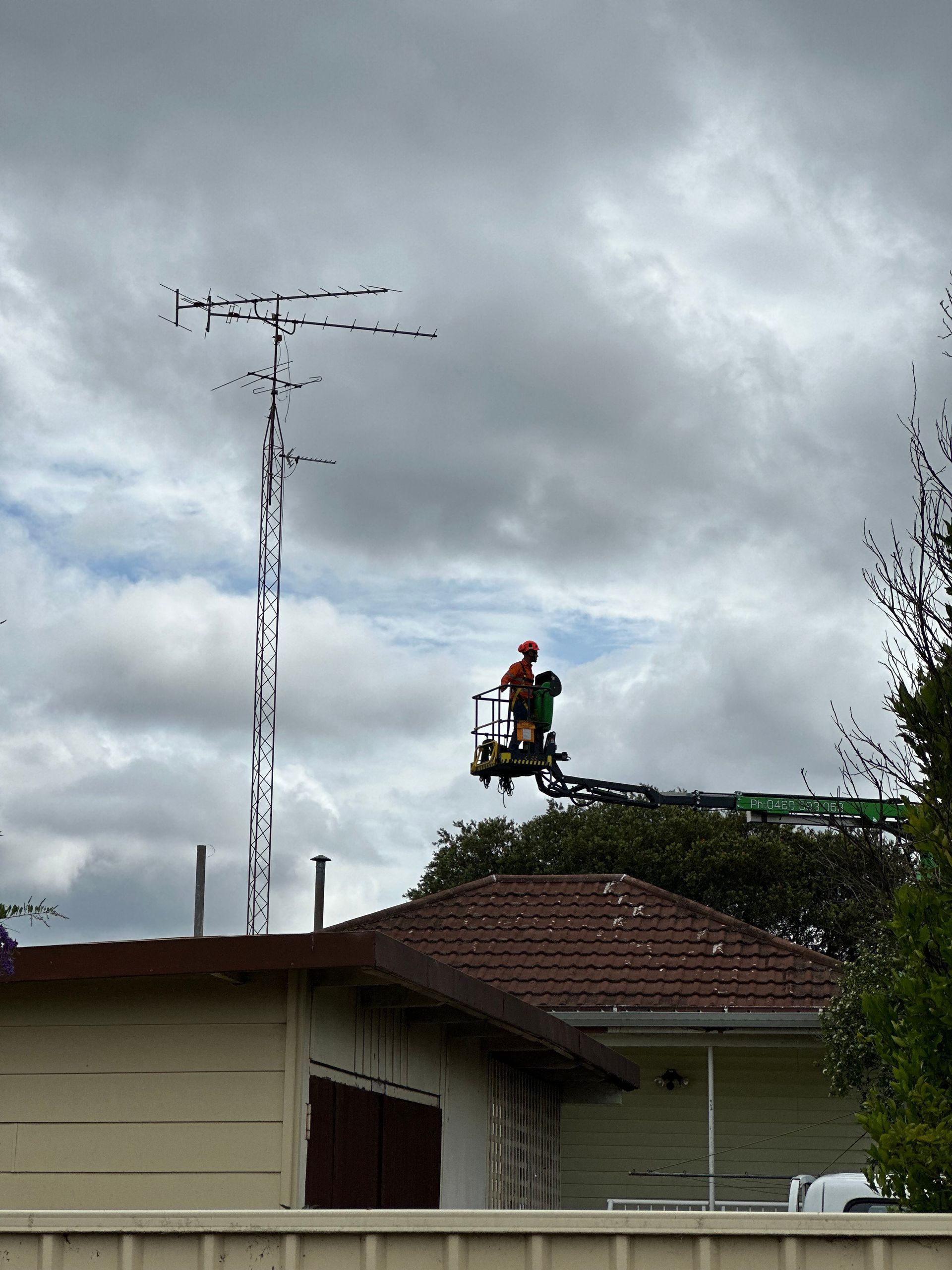 A Green Crane Is Working On An Antenna In Front Of A House — High Work Services in Maitland, NSW