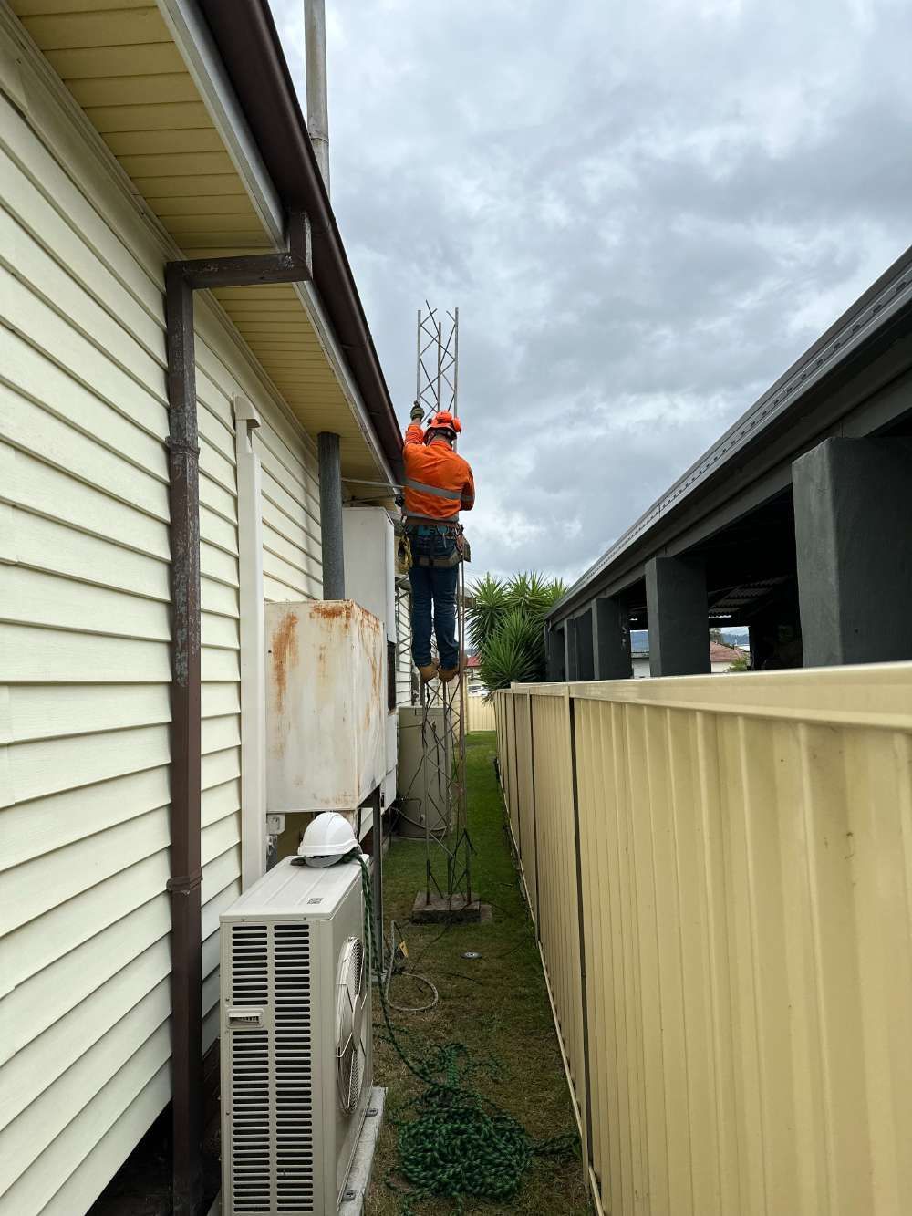 A Man Is Standing On A Ladder On The Side Of A Building — High Work Services in Maitland, NSW