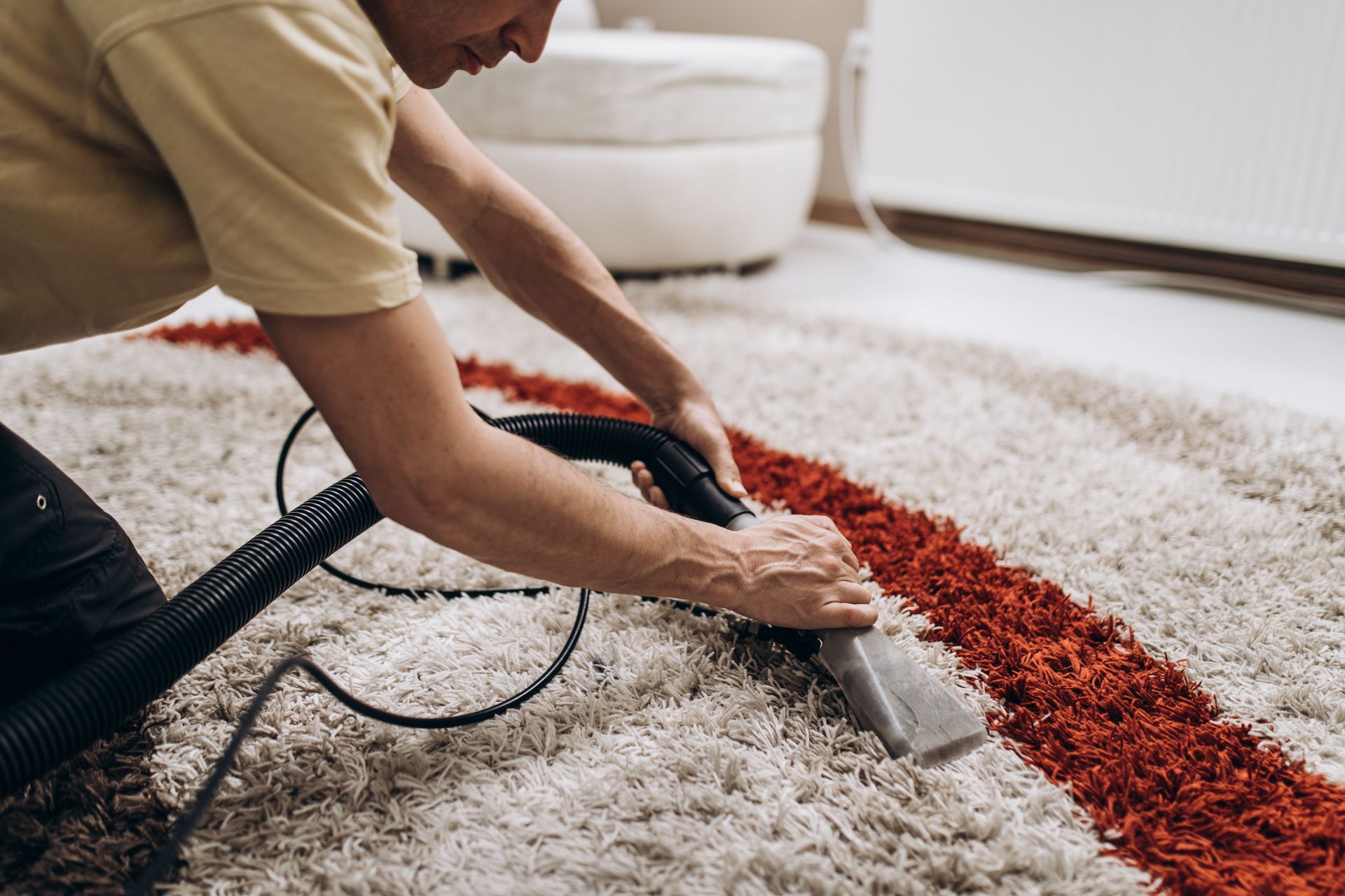 A person uses an extraction machine to deep clean a textured, white shag rug with a vibrant orange stripe.