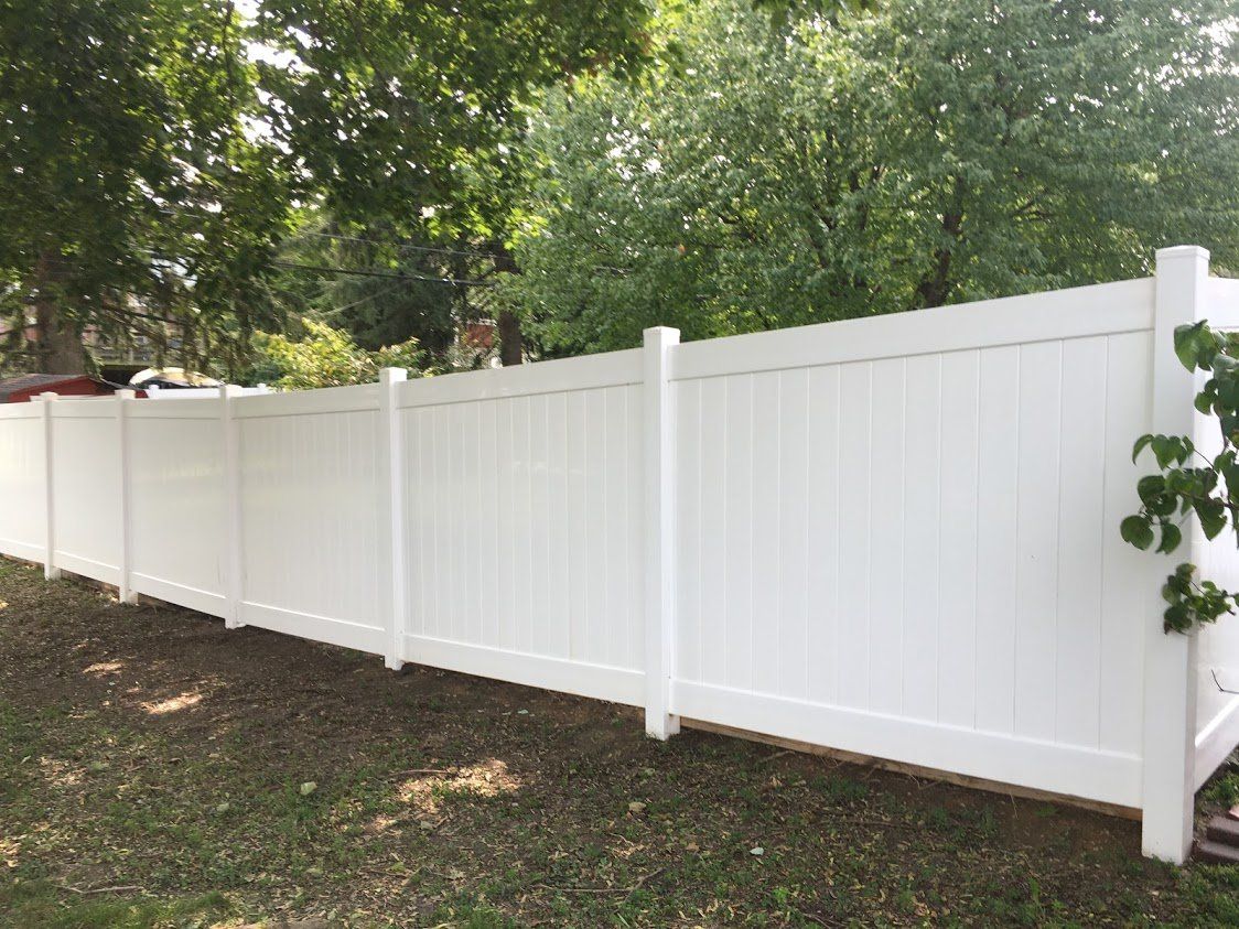 A white vinyl fence is surrounded by trees in a backyard.