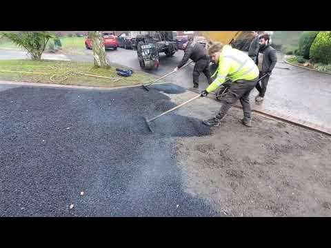 Workers paving a driveway with fresh asphalt, using rakes to spread the dark material.