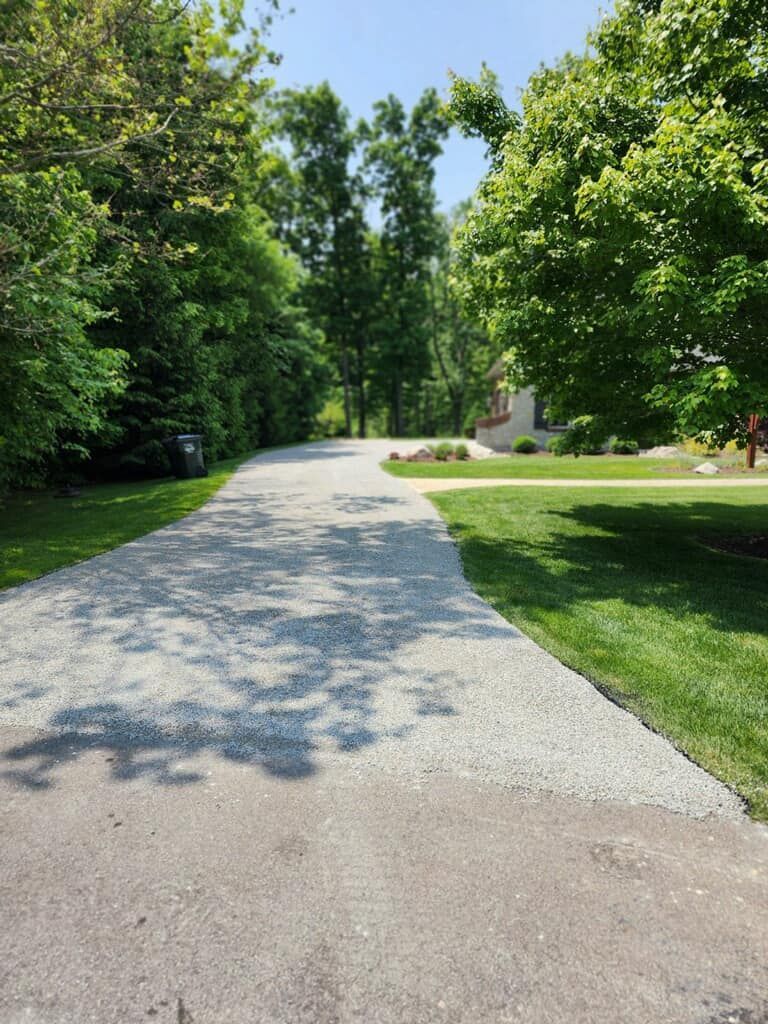 Gravel driveway curves through trees, leading to a house on a sunny day.
