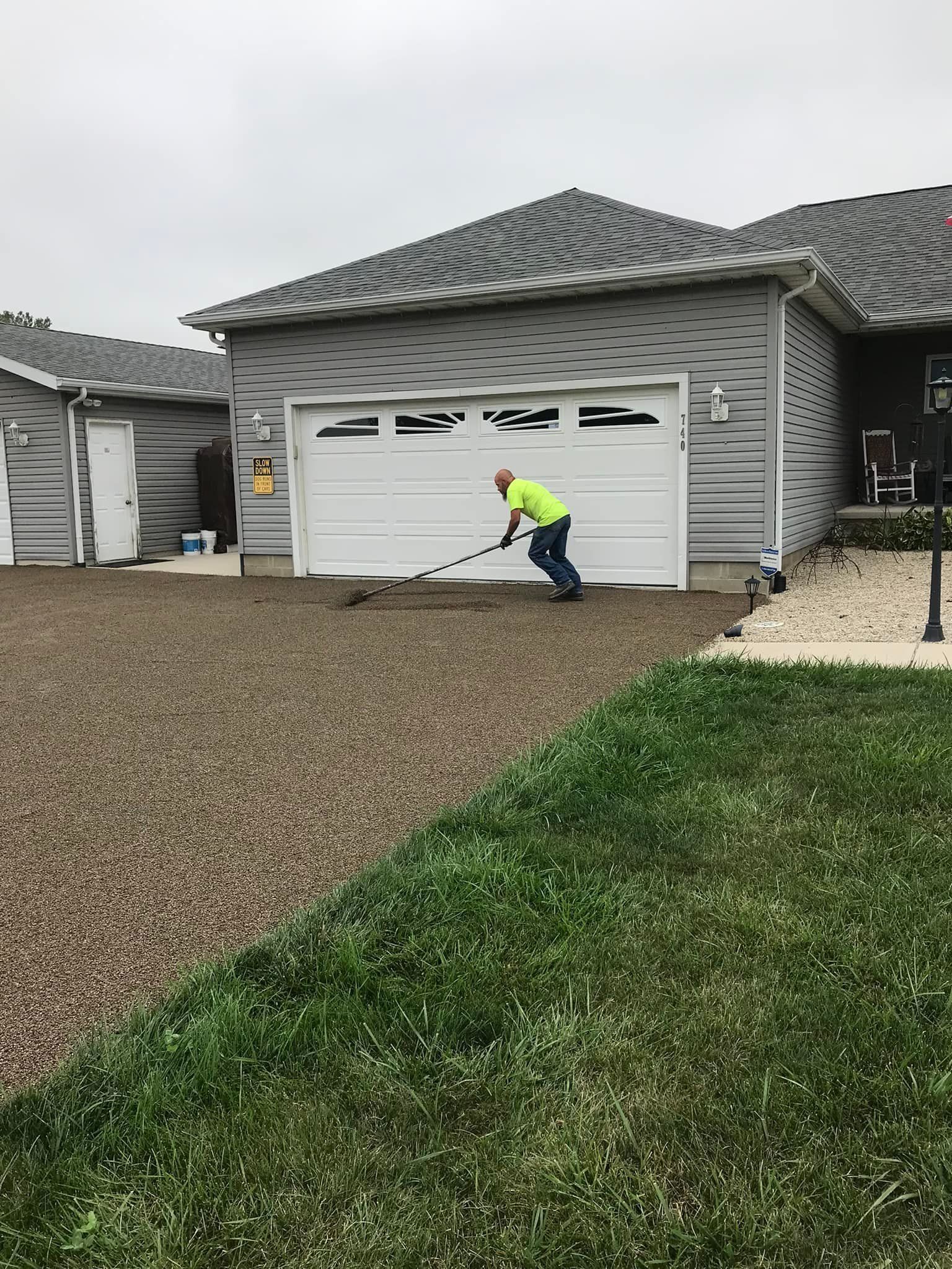 Man raking gravel driveway in front of a two-car garage on an overcast day.