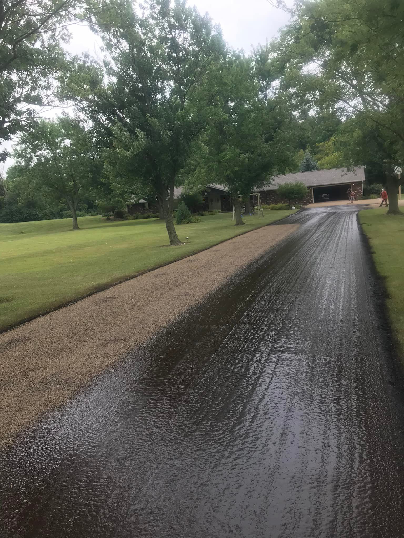 Asphalt driveway lined with gravel, trees on one side, house in the background.
