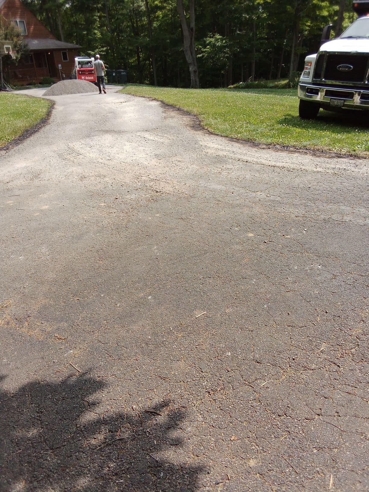 Asphalt driveway curves toward a house, a truck parked on grass.