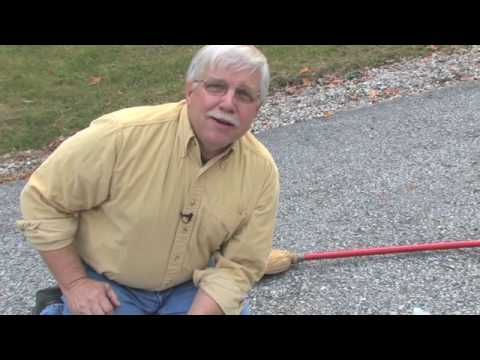Man kneeling outdoors on asphalt, gesturing towards a red-handled broom.